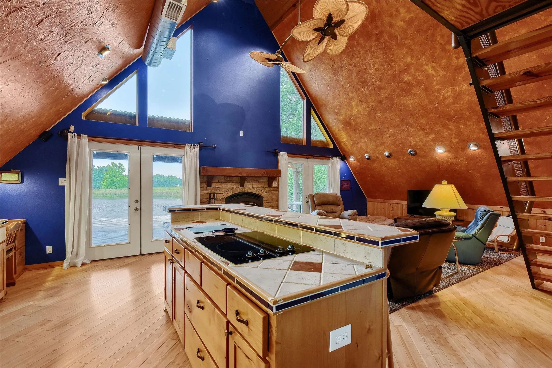 Kitchen featuring light hardwood / wood-style floors, black electric cooktop, a stone fireplace, tile countertops, and french doors