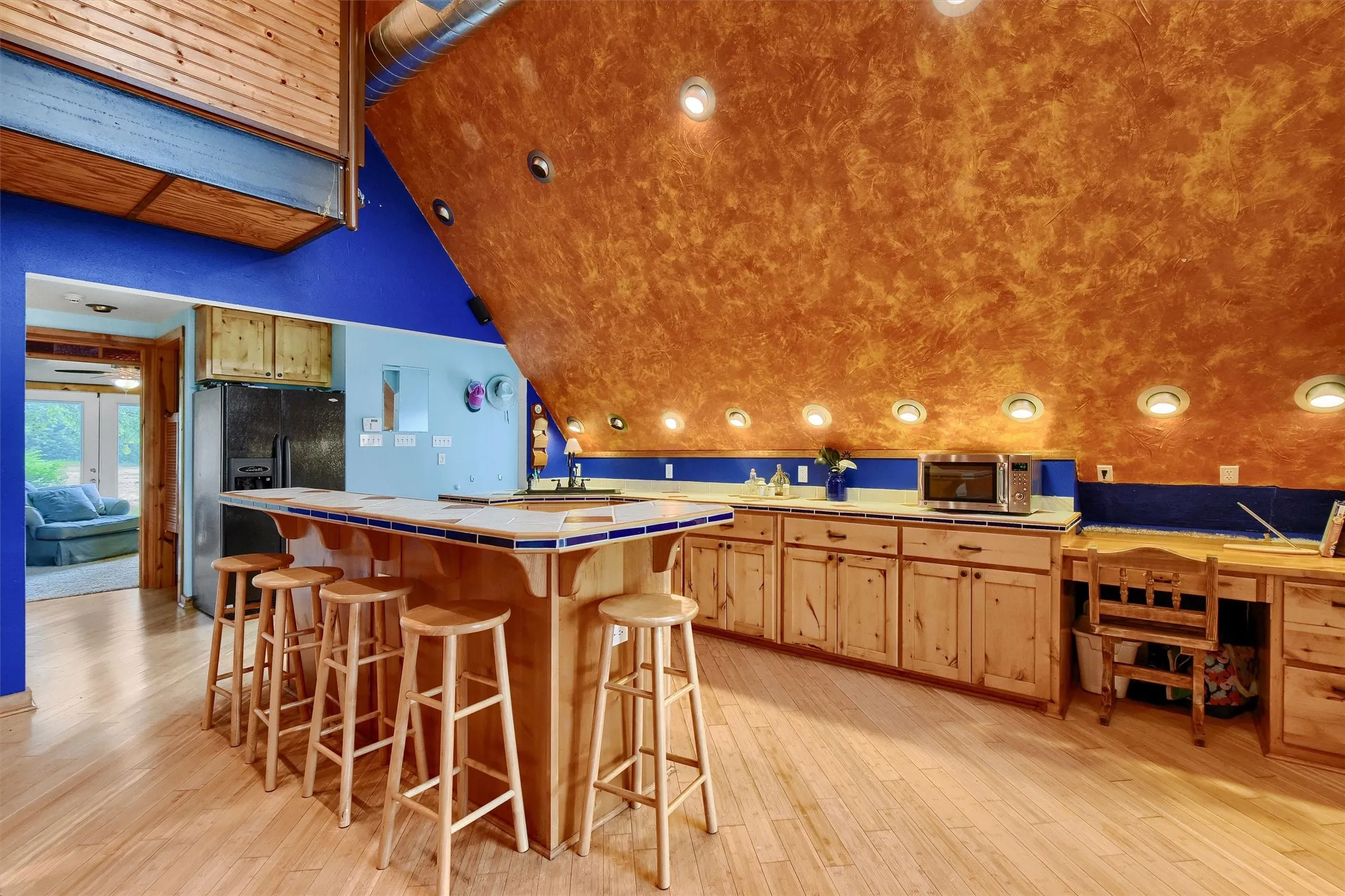 Kitchen with light brown cabinets, black fridge, tile countertops, a center island, and light wood-type flooring