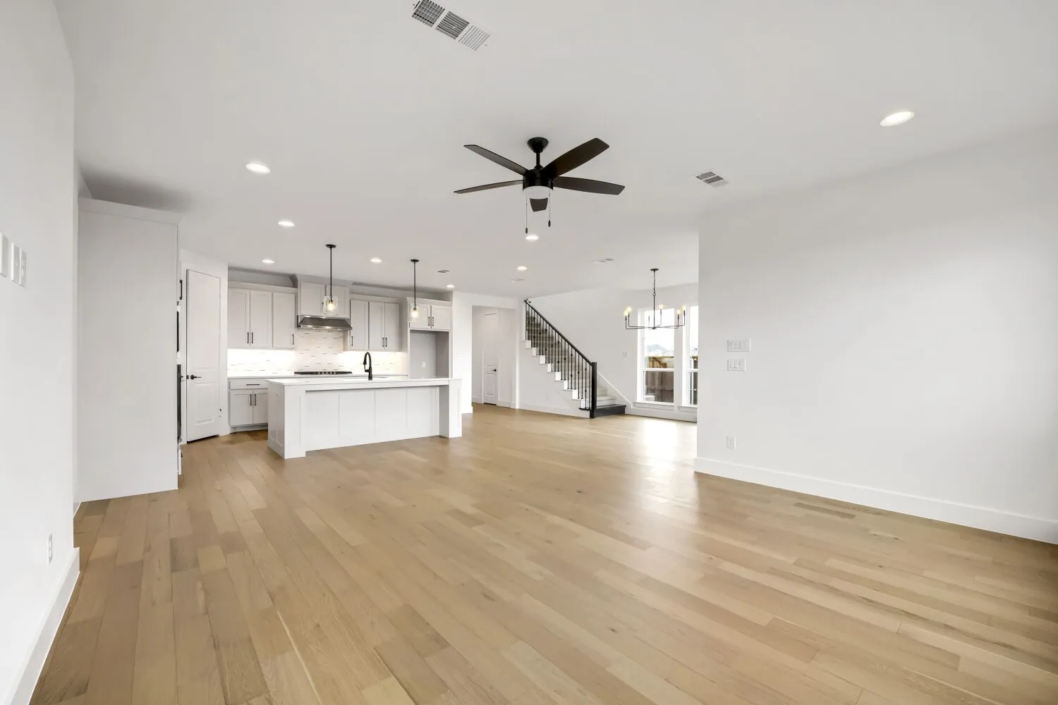 Expansive main living area featuring wood-finish flooring, a modern ceiling fan, recessed lighting, and a contemporary staircase with metal balusters