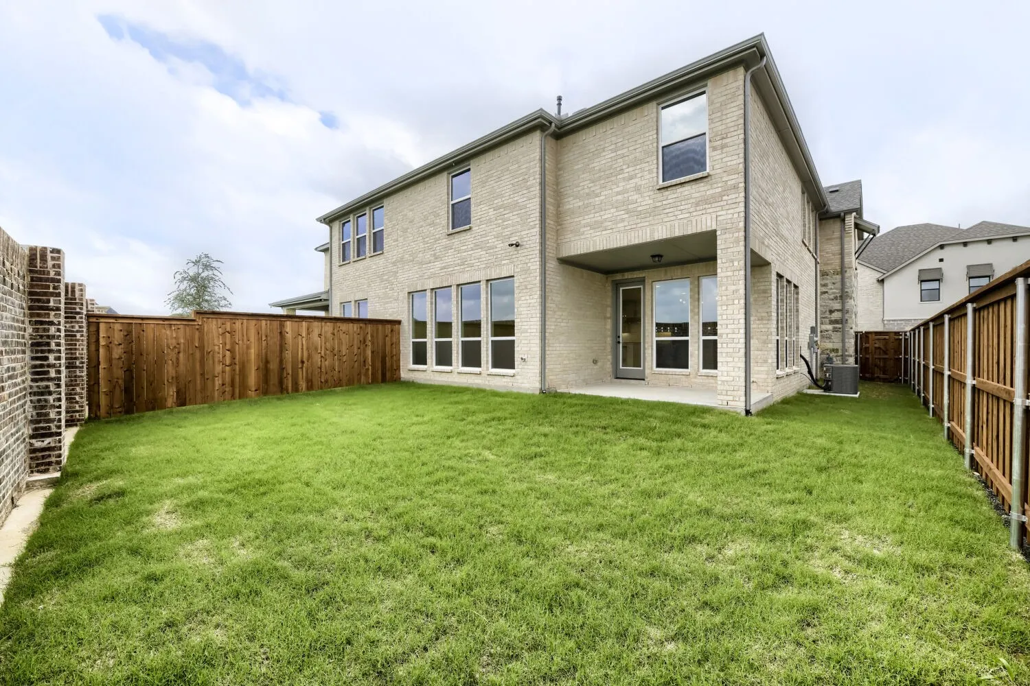 Expansive backyard featuring a manicured lawn, full privacy fencing, and a covered patio area