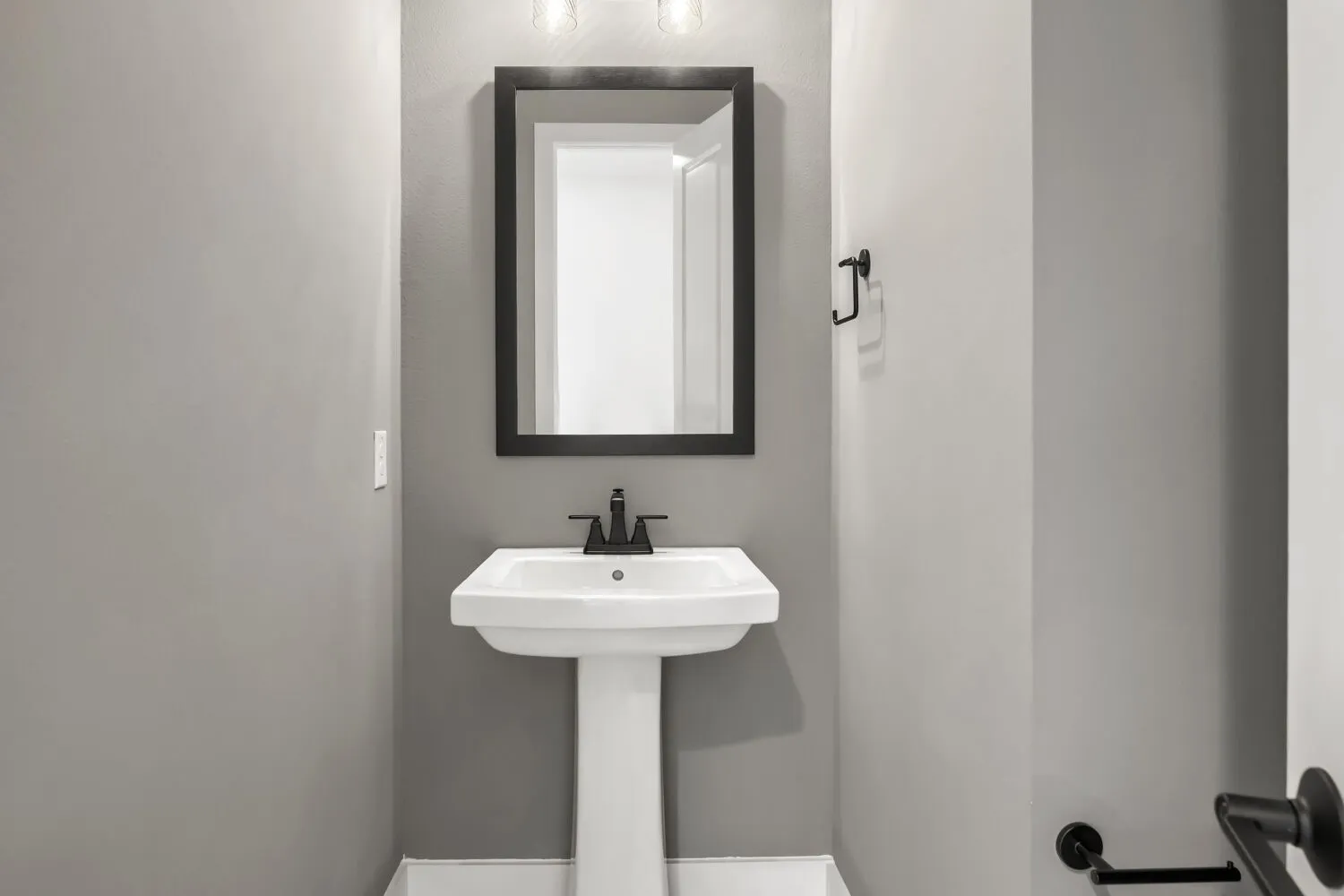 Pedestal sink with matte black faucet, framed mirror, and wall-mounted light fixture