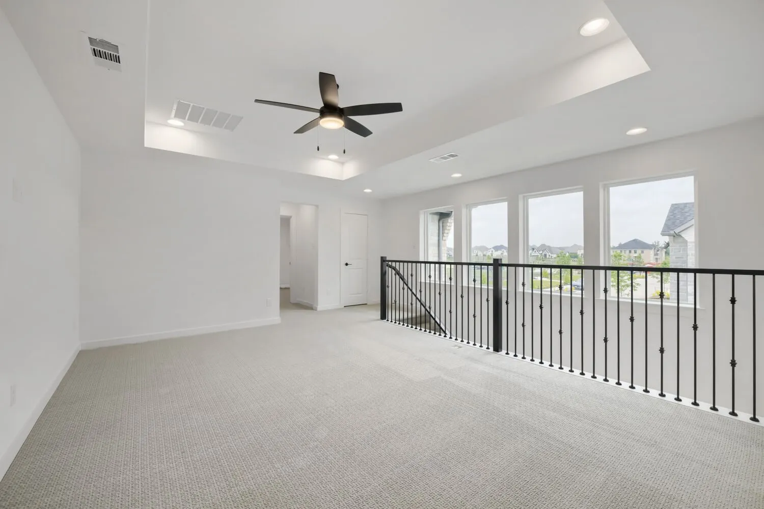 Expansive carpeted area featuring a tray ceiling, recessed lighting, and a ceiling fan