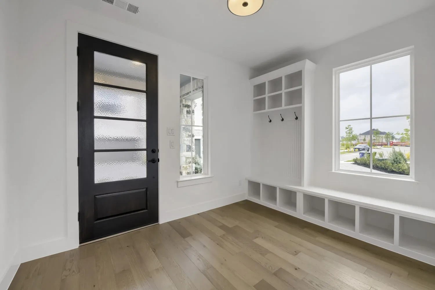 Wood-finish flooring, built-in storage bench, built-in shelving, white trim, and a black paneled door with textured glass inserts