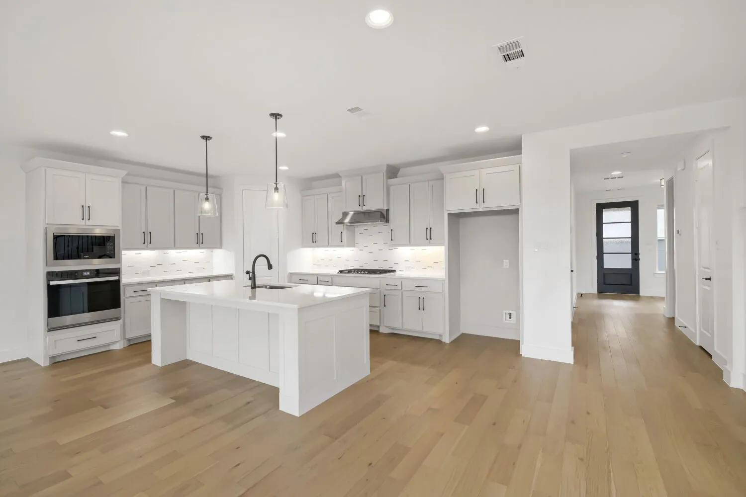 Kitchen featuring light wood-finish flooring, white cabinetry, a large central island with a sink, and stainless steel appliances