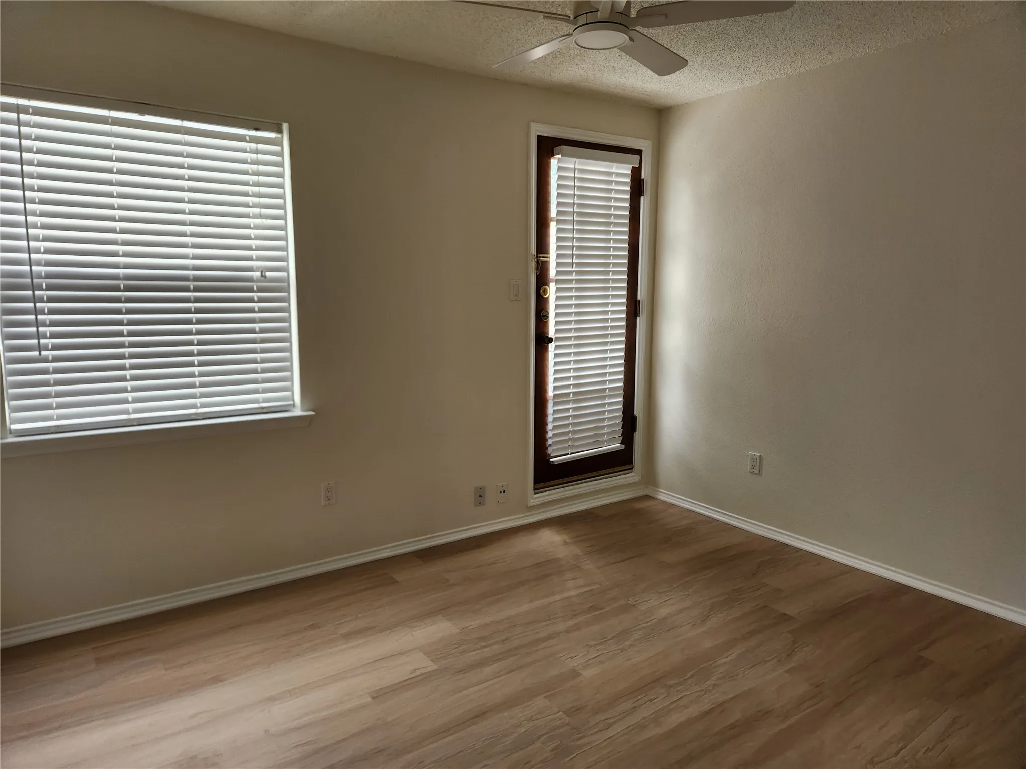 Wood-finish flooring with a dark wood staircase railing, featuring a window with white louvered shutters and a ceiling fan