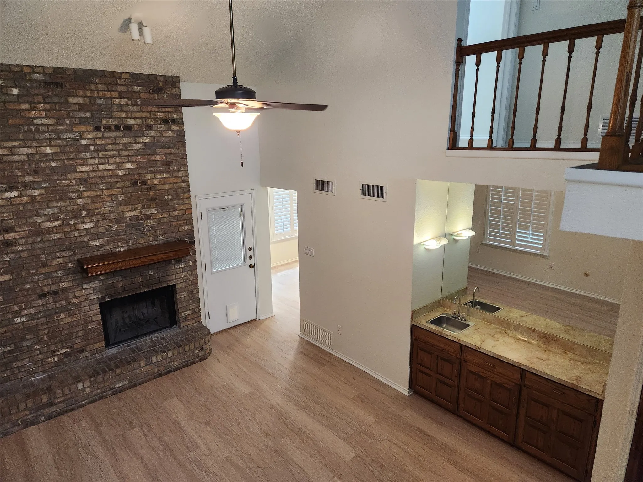 Vaulted ceiling, brick fireplace with wood mantel, wood-finish flooring, built-in wet bar with dual sinks and stone countertop, and upper-level railing