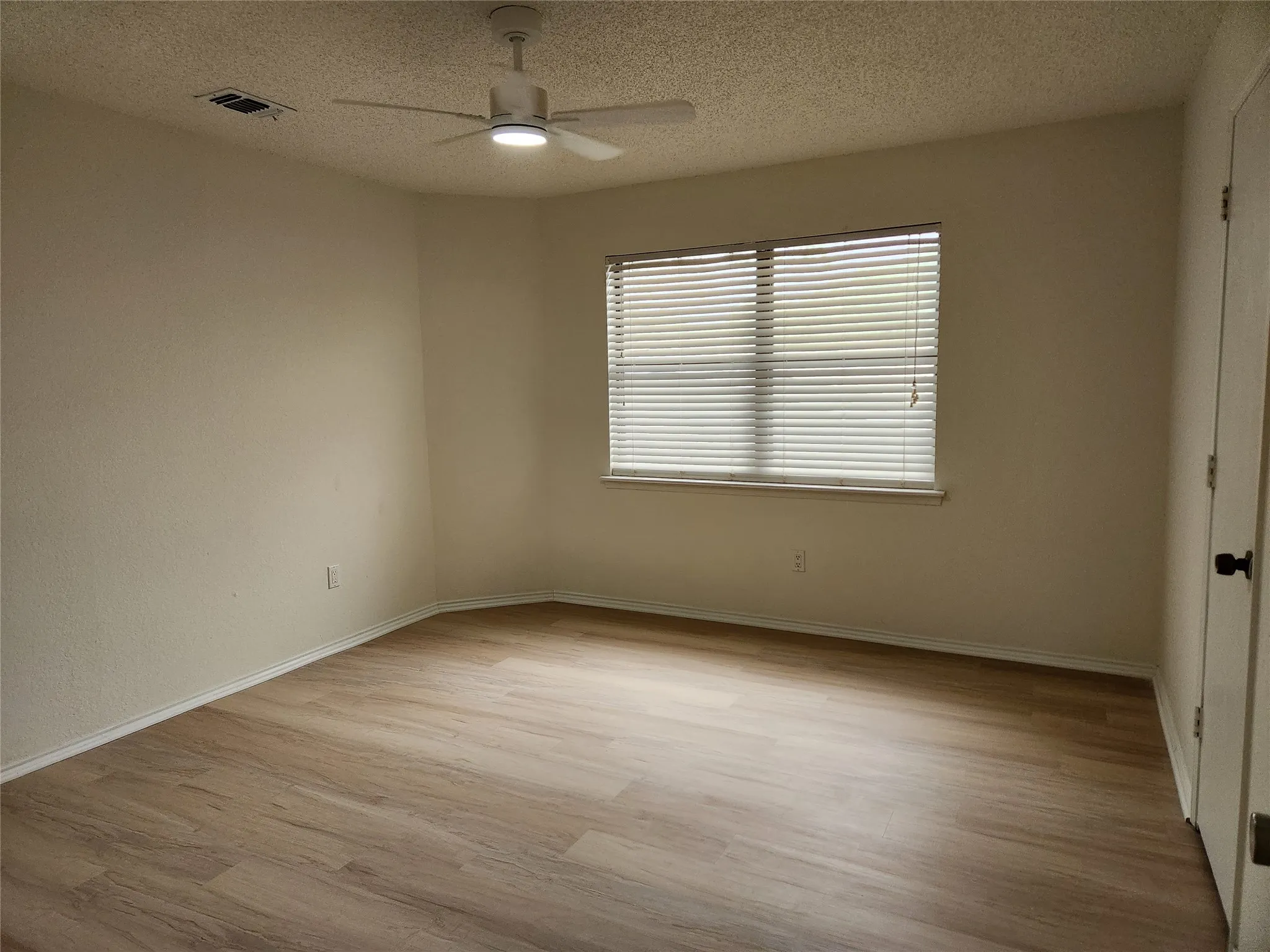 Wood-finish flooring, ceiling fan, white wall paint, window with blinds, and a glass-paneled door