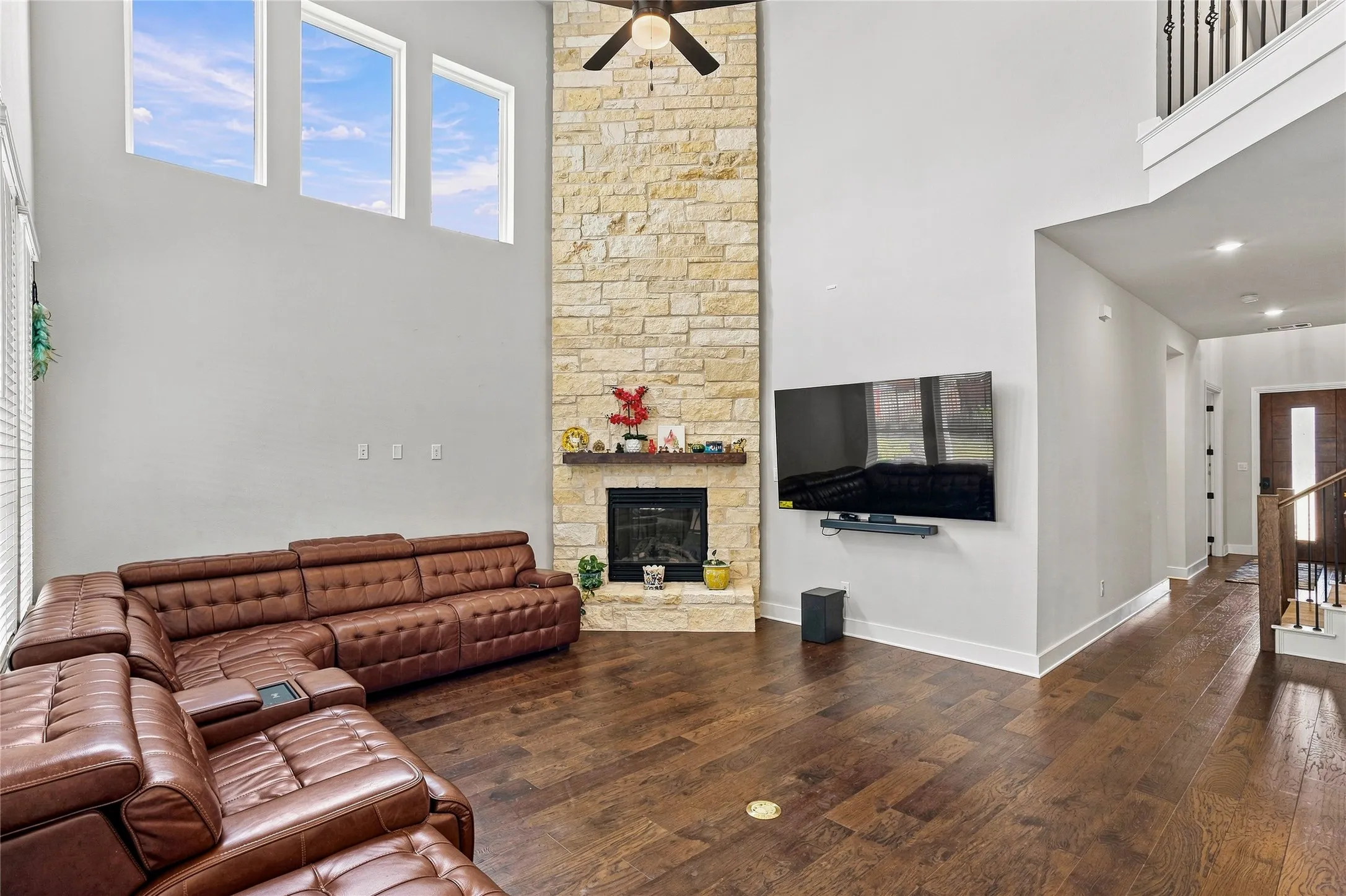 Two-story living area with high ceilings, wood-finish flooring, and a stacked stone fireplace with a wood mantle