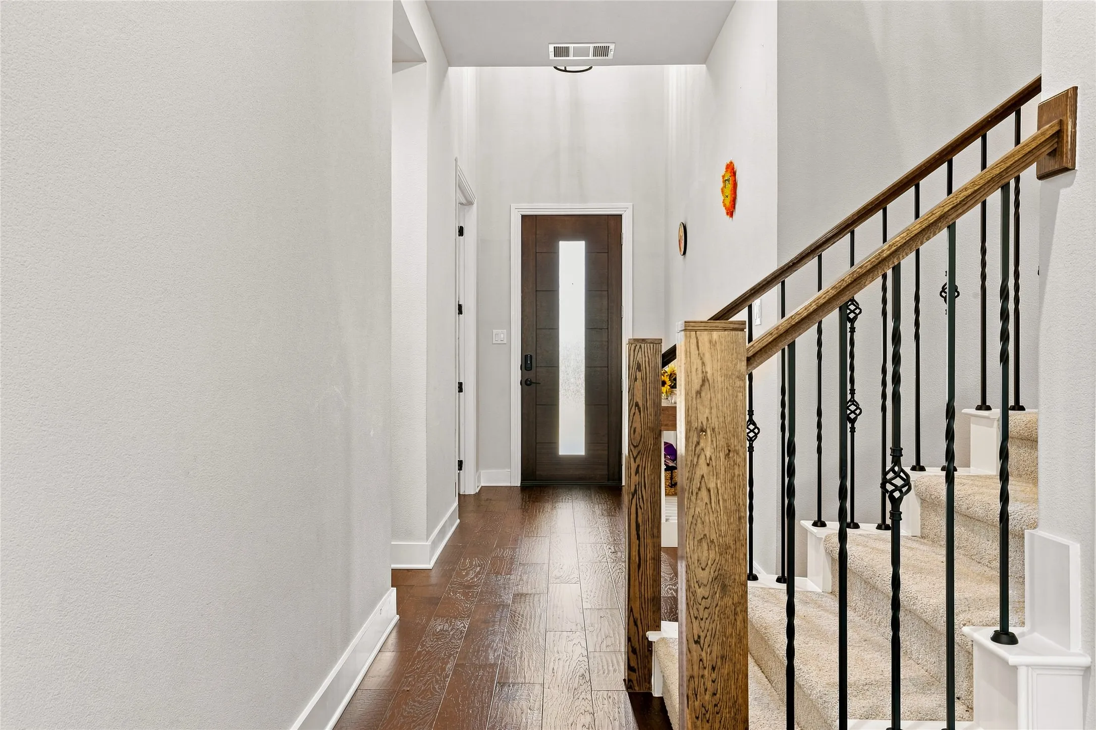 Entryway featuring wood-finish flooring, a dark wood entry door with a vertical frosted glass insert, and a staircase with wrought iron balusters and wood handrails