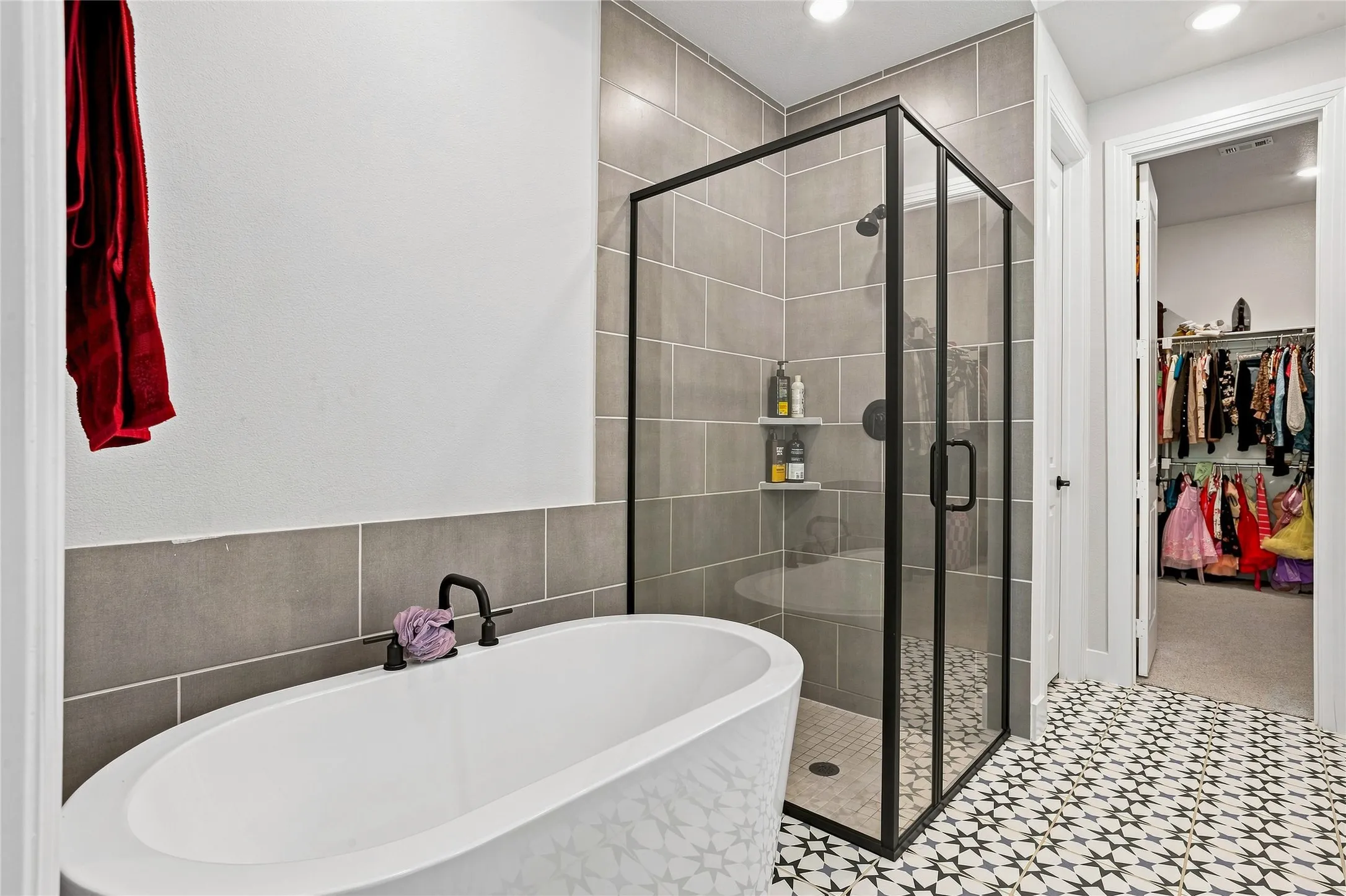 Freestanding soaking tub with matte black fixtures, glass-enclosed shower with tile surround, and patterned floor tile