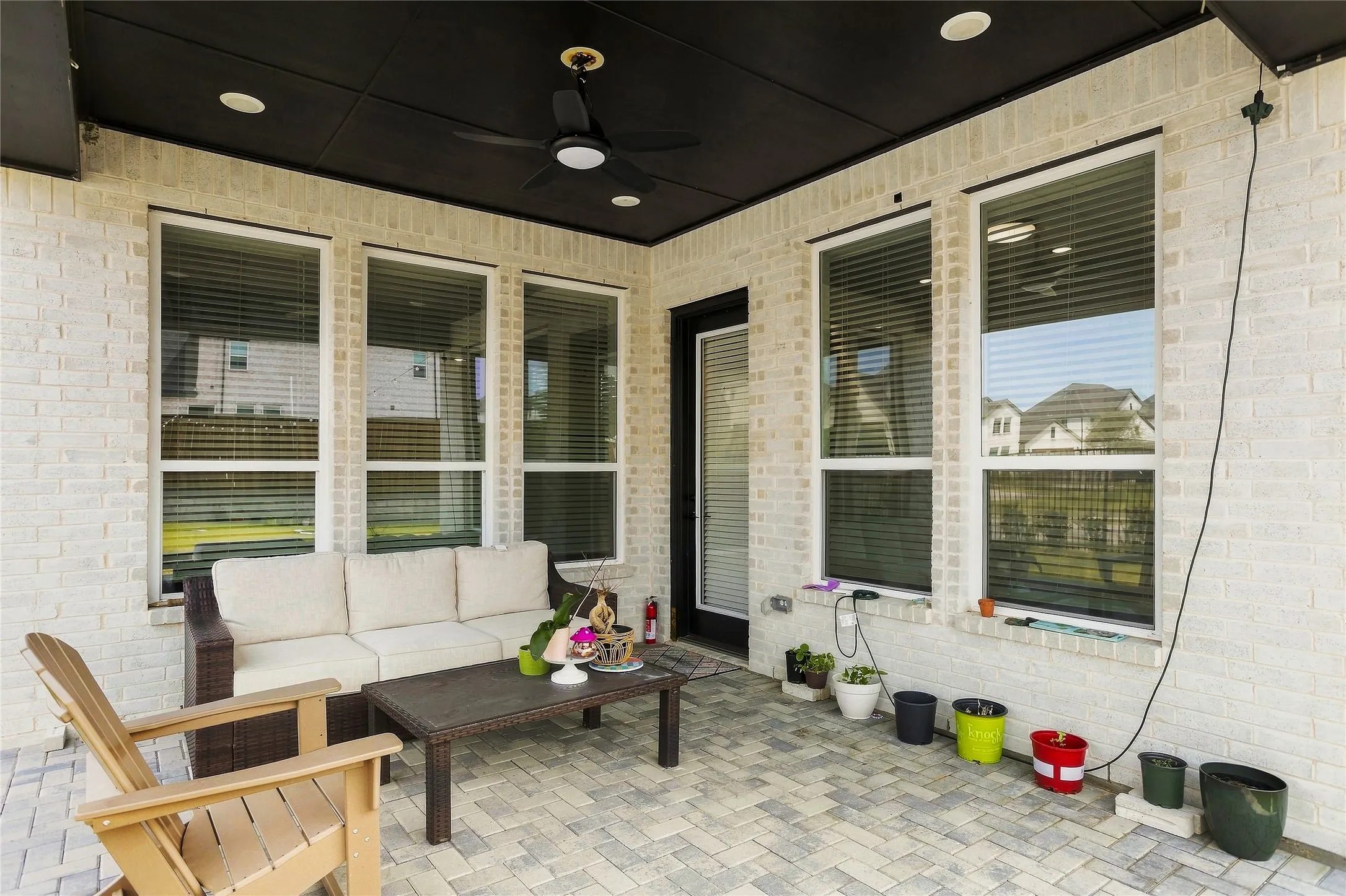 Covered outdoor patio featuring light-colored brick, a dark ceiling with recessed lighting, a ceiling fan, and paver flooring