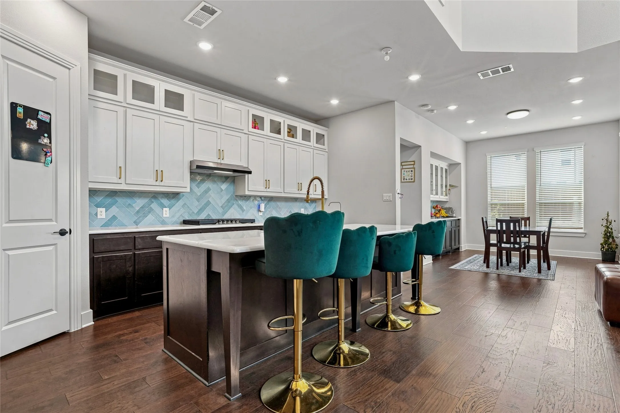Expansive kitchen island with a stone countertop, featuring a herringbone tile backsplash, stainless steel range hood, and recessed lighting