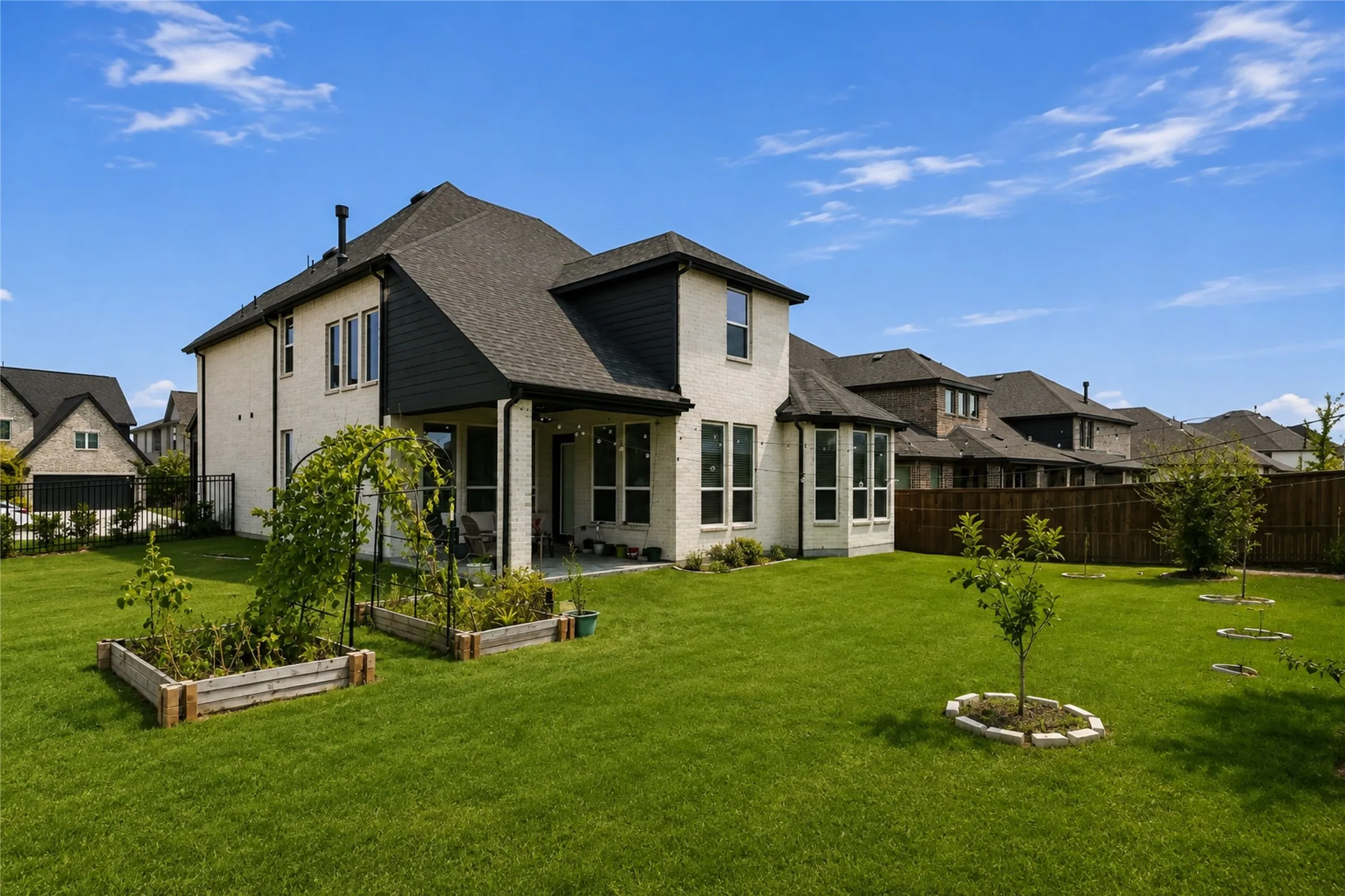 Expansive green lawn, covered patio, raised garden beds, wood fence, and a multi-level exterior