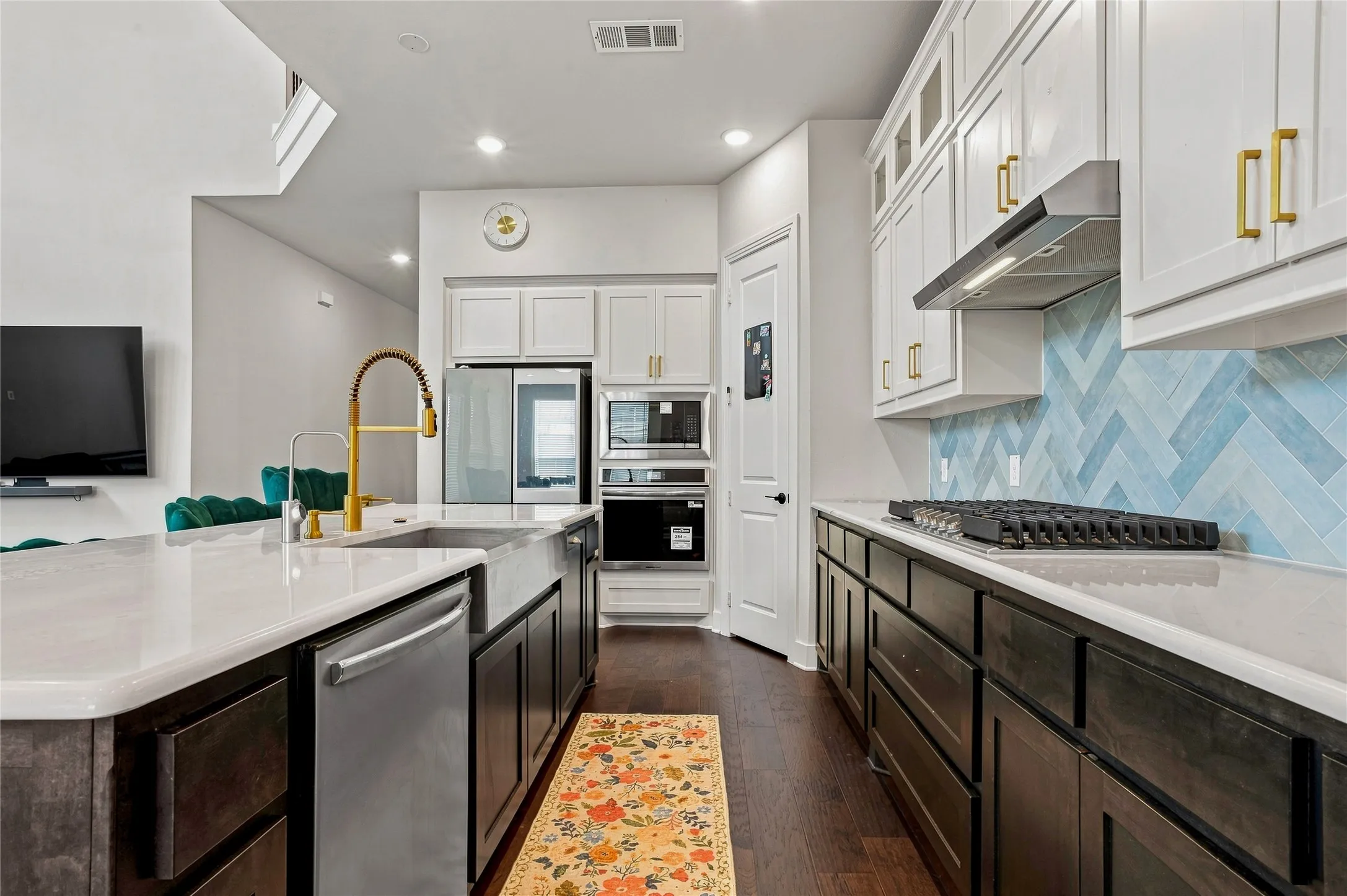 Kitchen featuring wood-finish flooring, white countertops, built-in stainless steel appliances, a herringbone tile backsplash, and a gold-finish faucet