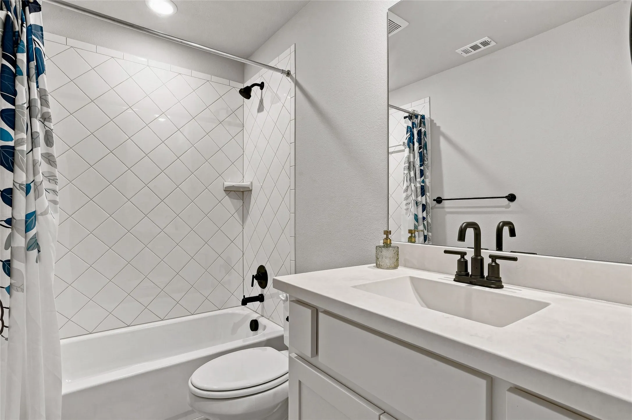White subway tile shower surround with diagonal pattern, white bathtub, vanity with integrated sink, matte black faucet, and frameless mirror