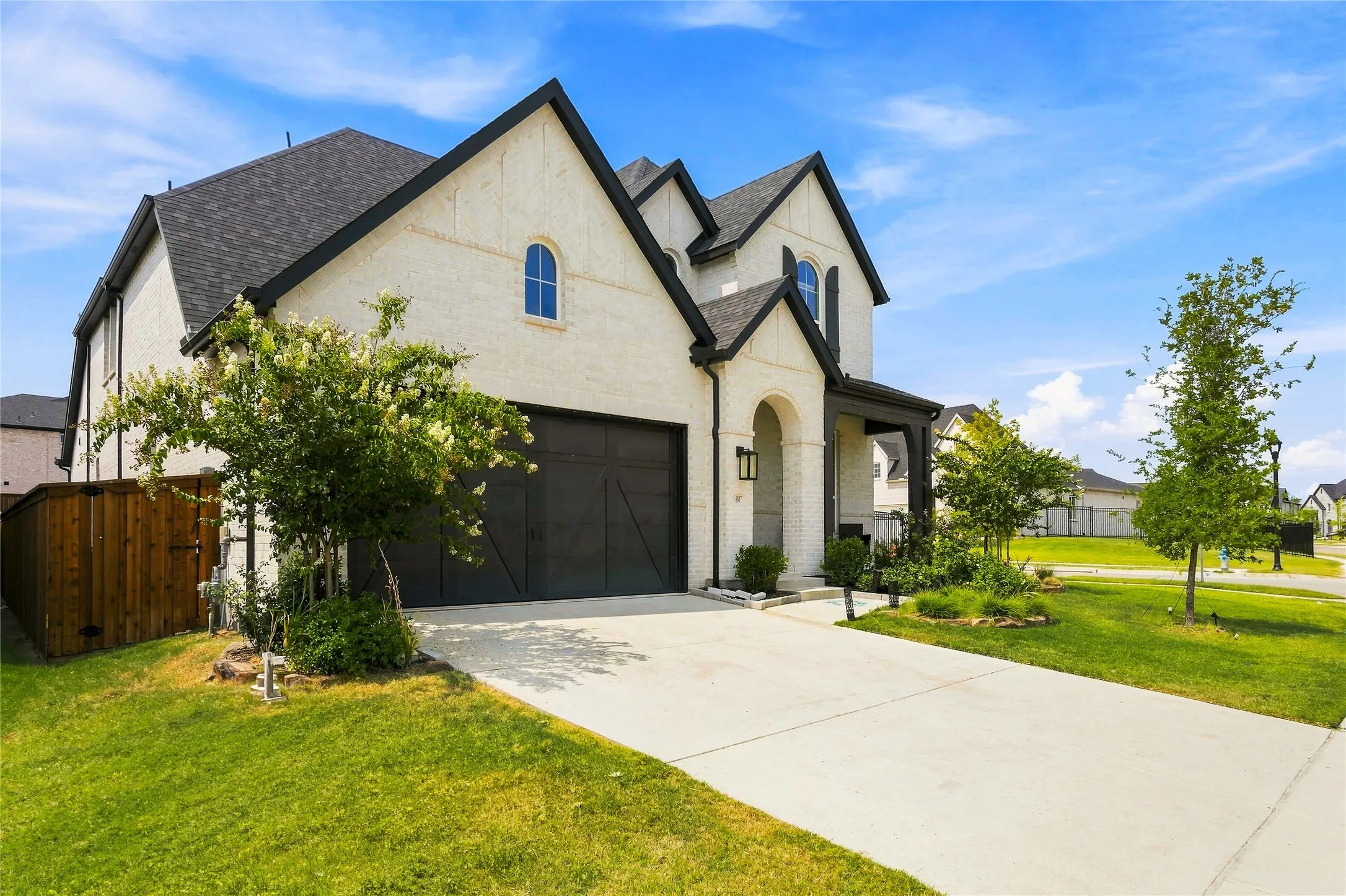 Cream-colored brick exterior with black trim, an arched entry, a two-car garage, and an extended driveway