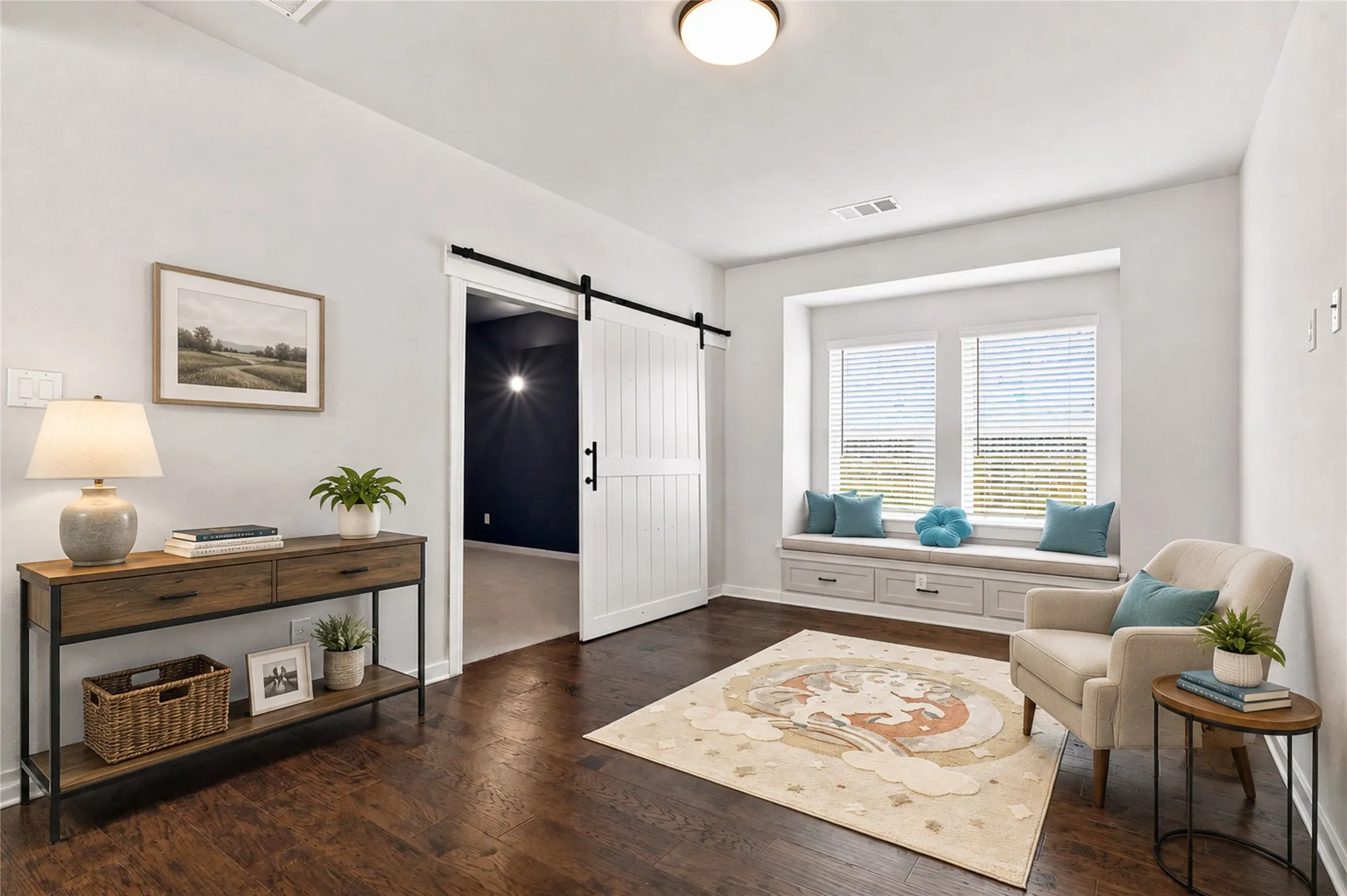Dark wood-finish flooring, white barn door with black hardware, built-in window seat with storage, white trim, and a prominent window virtul staged