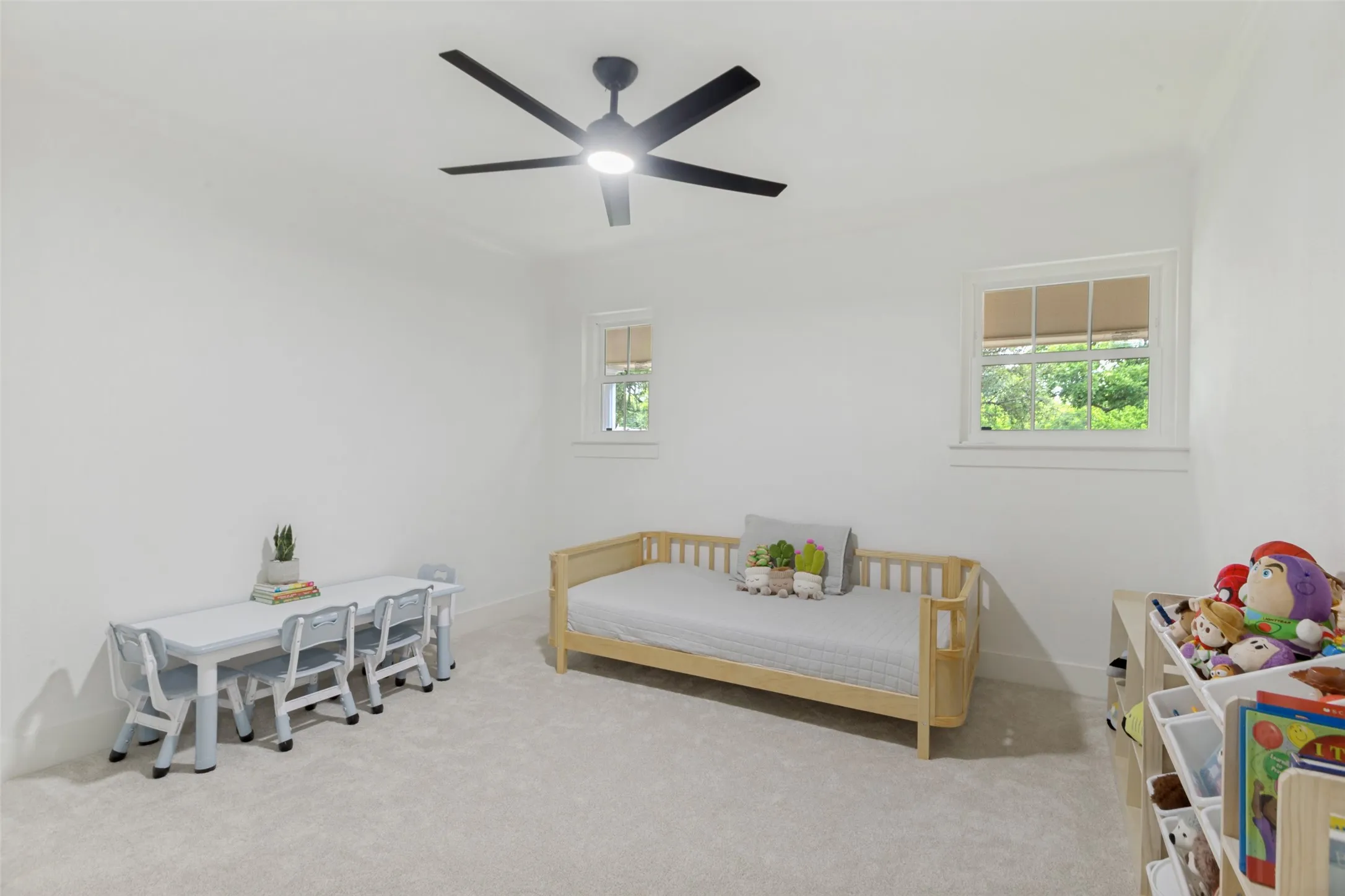 Recessed lighting and a ceiling fan fixture illuminate a room featuring two windows with white trim, and light-colored carpeting