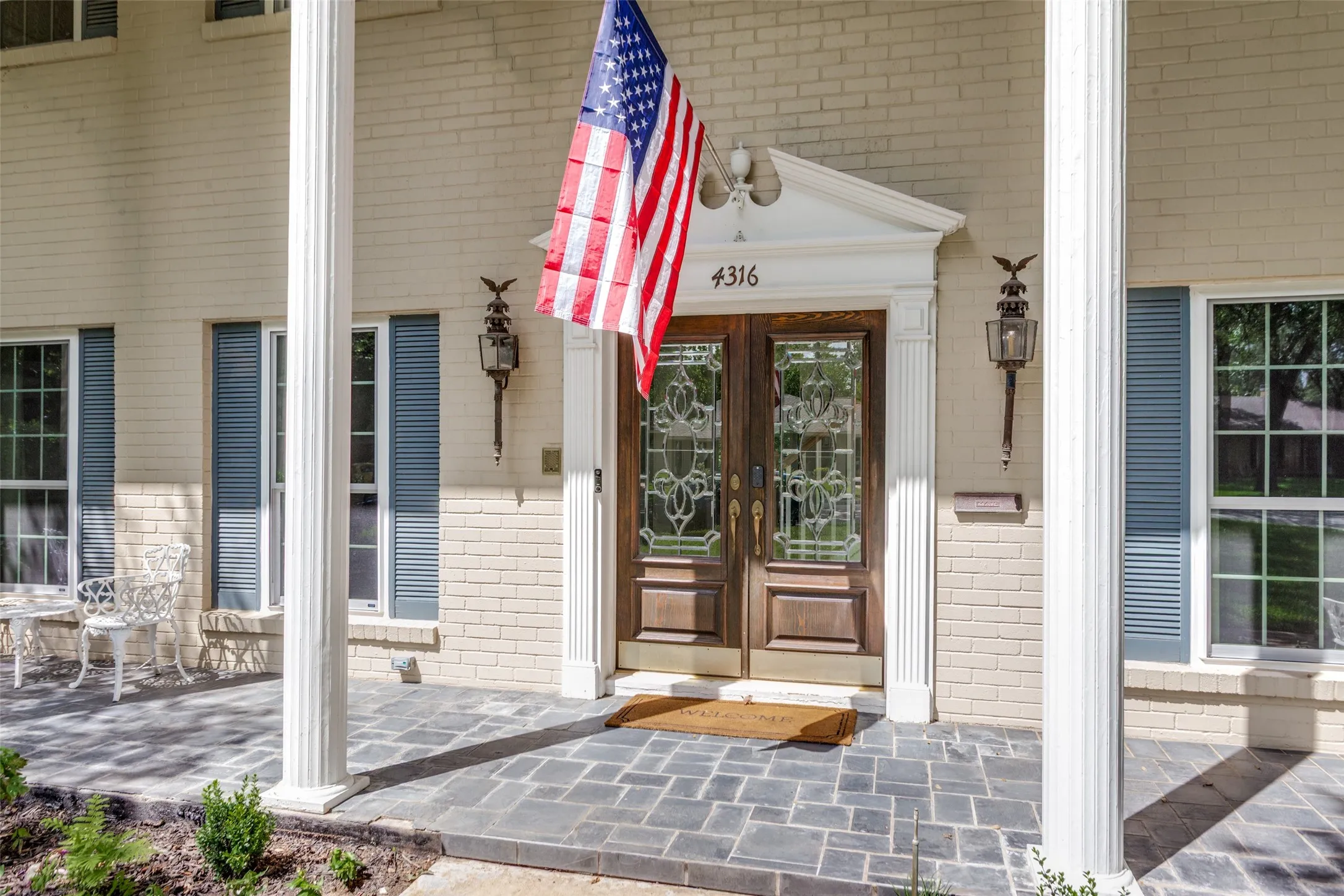 Cream brick exterior with decorative columns, a slate tile porch, and a double entry door with ornate glass inserts
