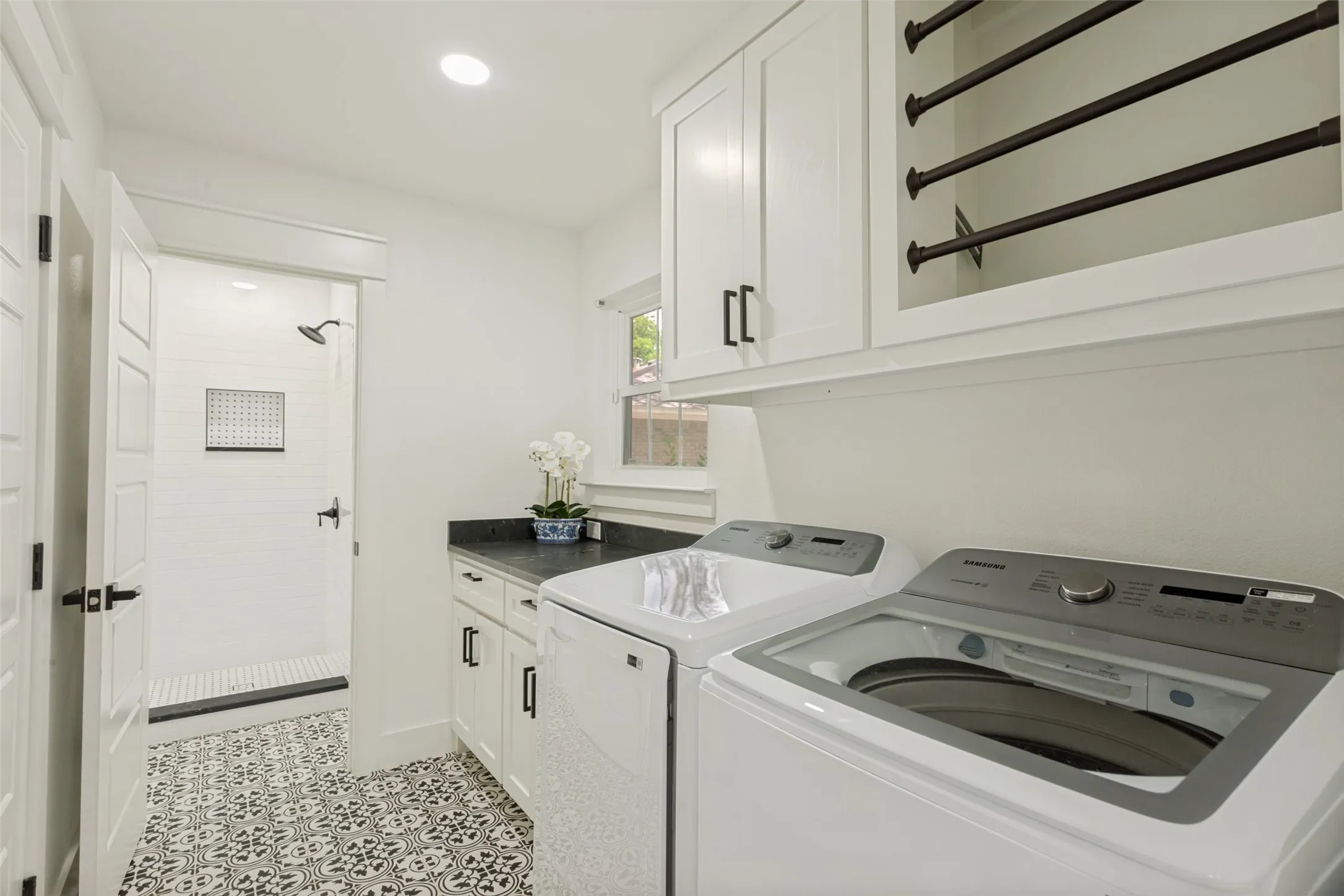 Laundry room with a patterned tile floor, white shaker-style cabinetry, dark countertop, and a built-in shower with white subway tile