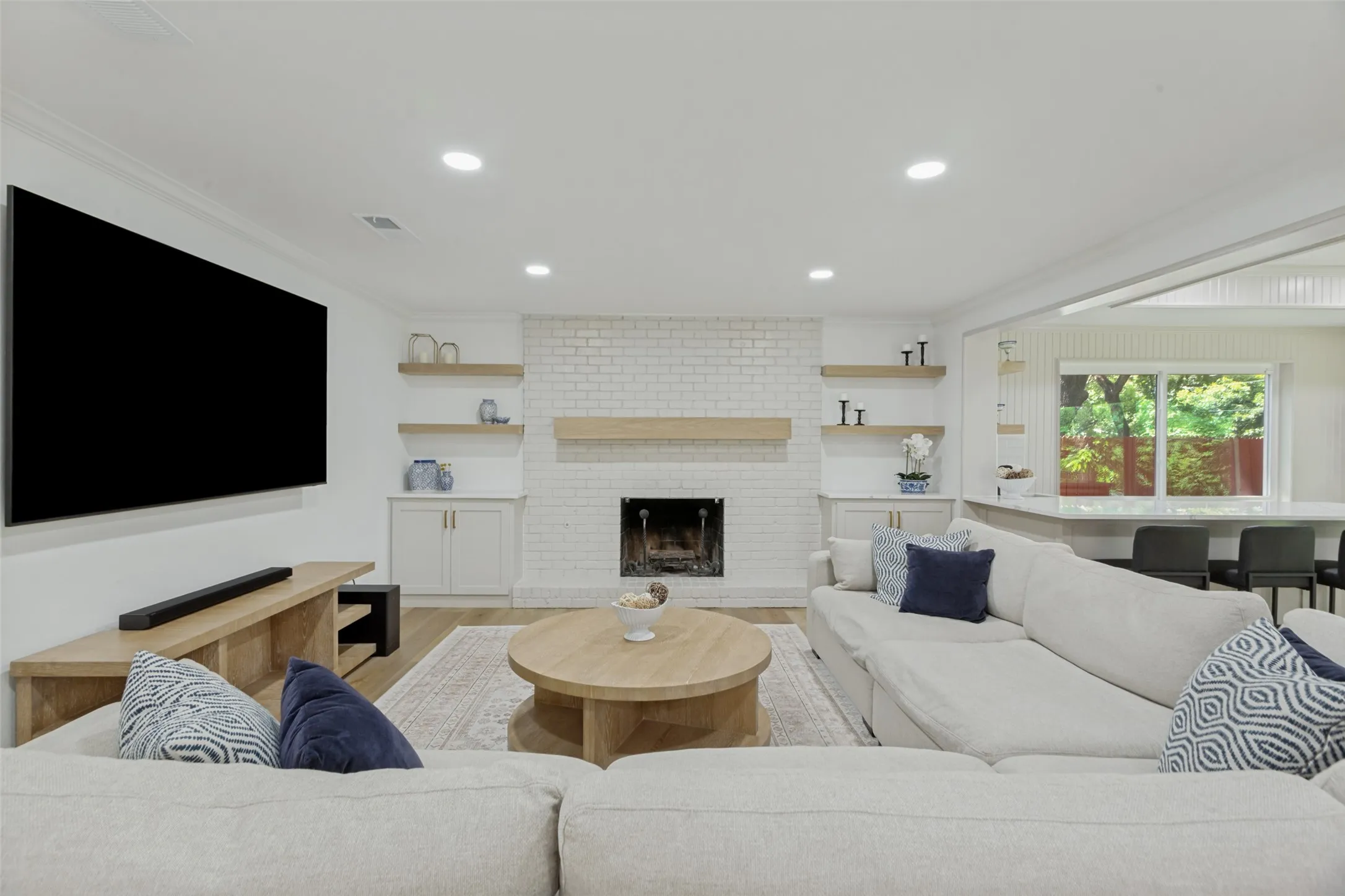White brick fireplace with a wood mantle and hearth, flanked by built-in cabinetry and floating wood shelves