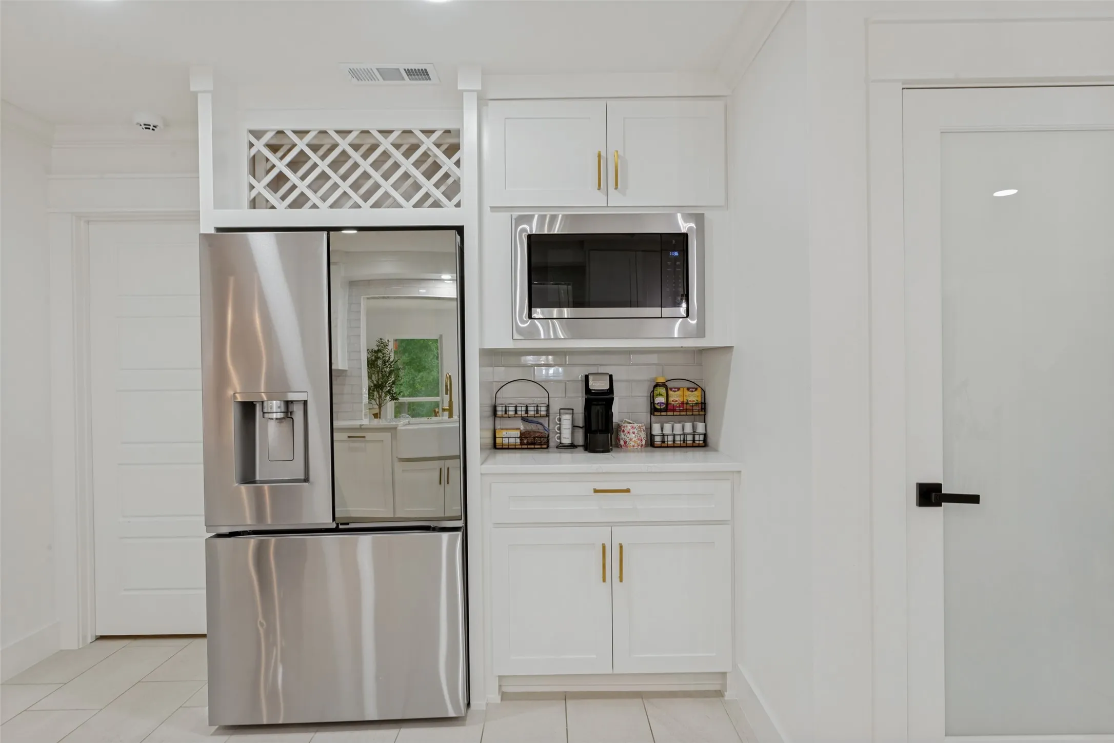Stainless steel refrigerator, white cabinetry with gold-tone hardware, built-in microwave, white subway tile backsplash, and frosted glass door with black hardware