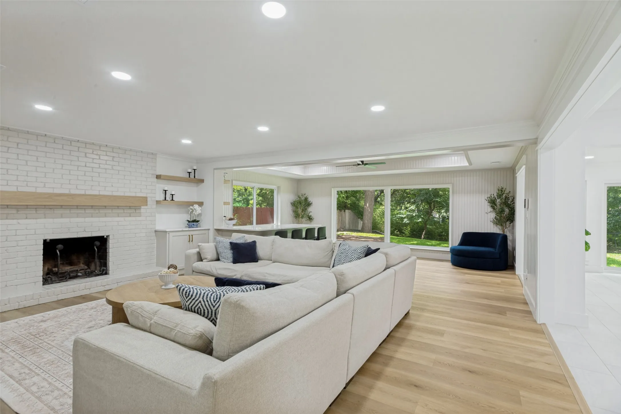 White brick fireplace with wood mantel, built-in cabinetry, recessed lighting, wood-finish flooring, and expansive windows