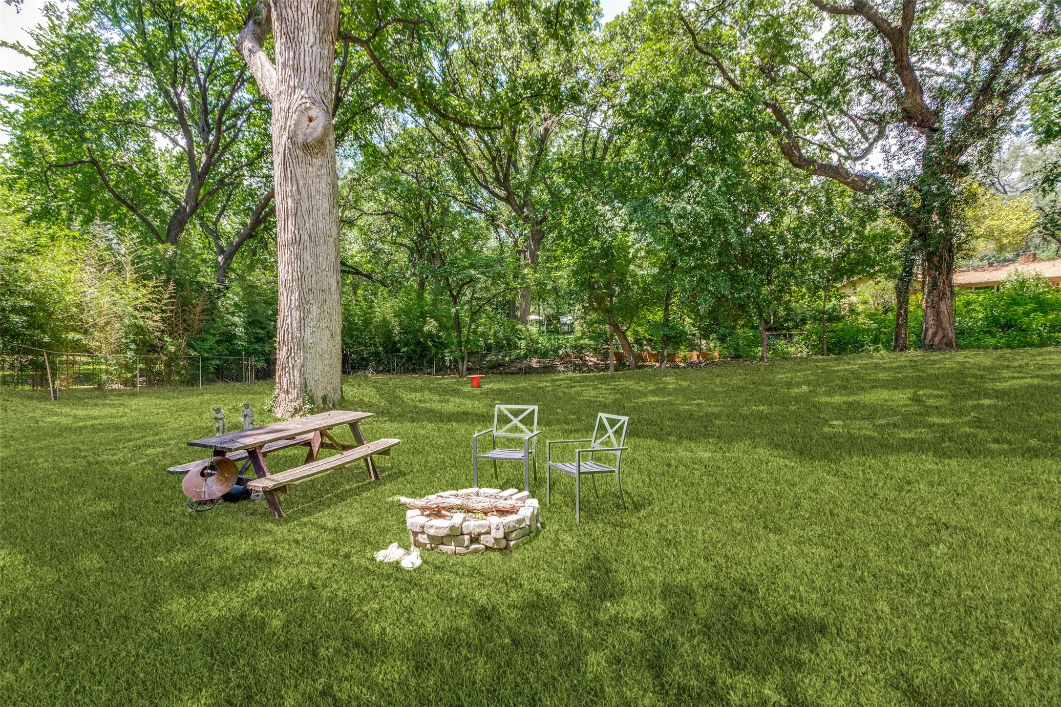 Expansive green lawn with mature trees, a stone-lined fire pit, and a picnic table