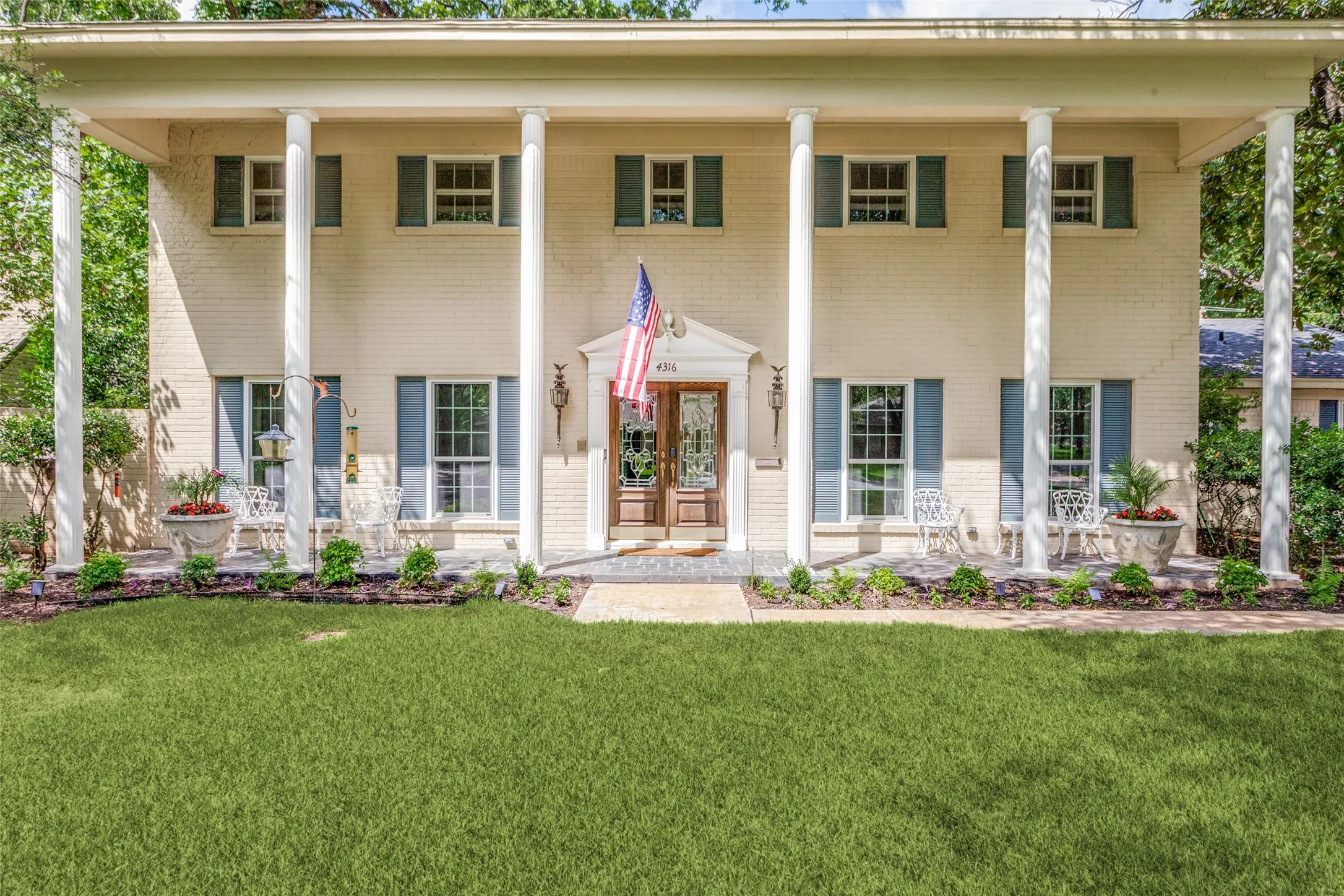 Two-story light brick exterior with a columned front porch, framed by mature trees