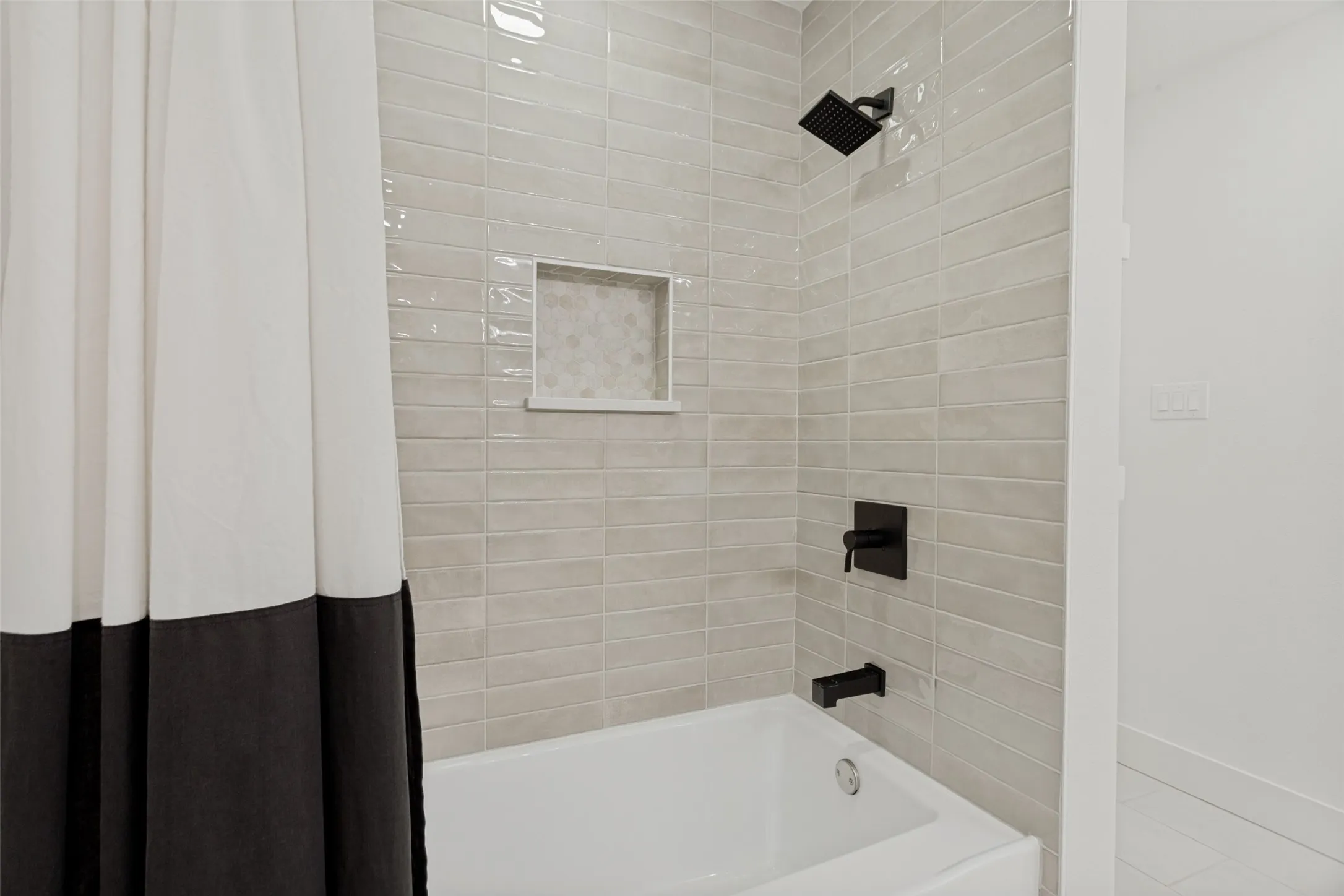 Subway tile shower surround with matte black fixtures and a recessed niche
