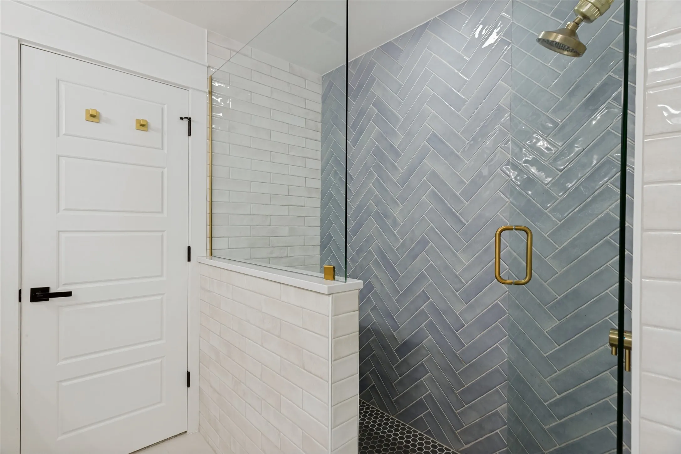 Frameless glass shower enclosure with a herringbone tile accent wall