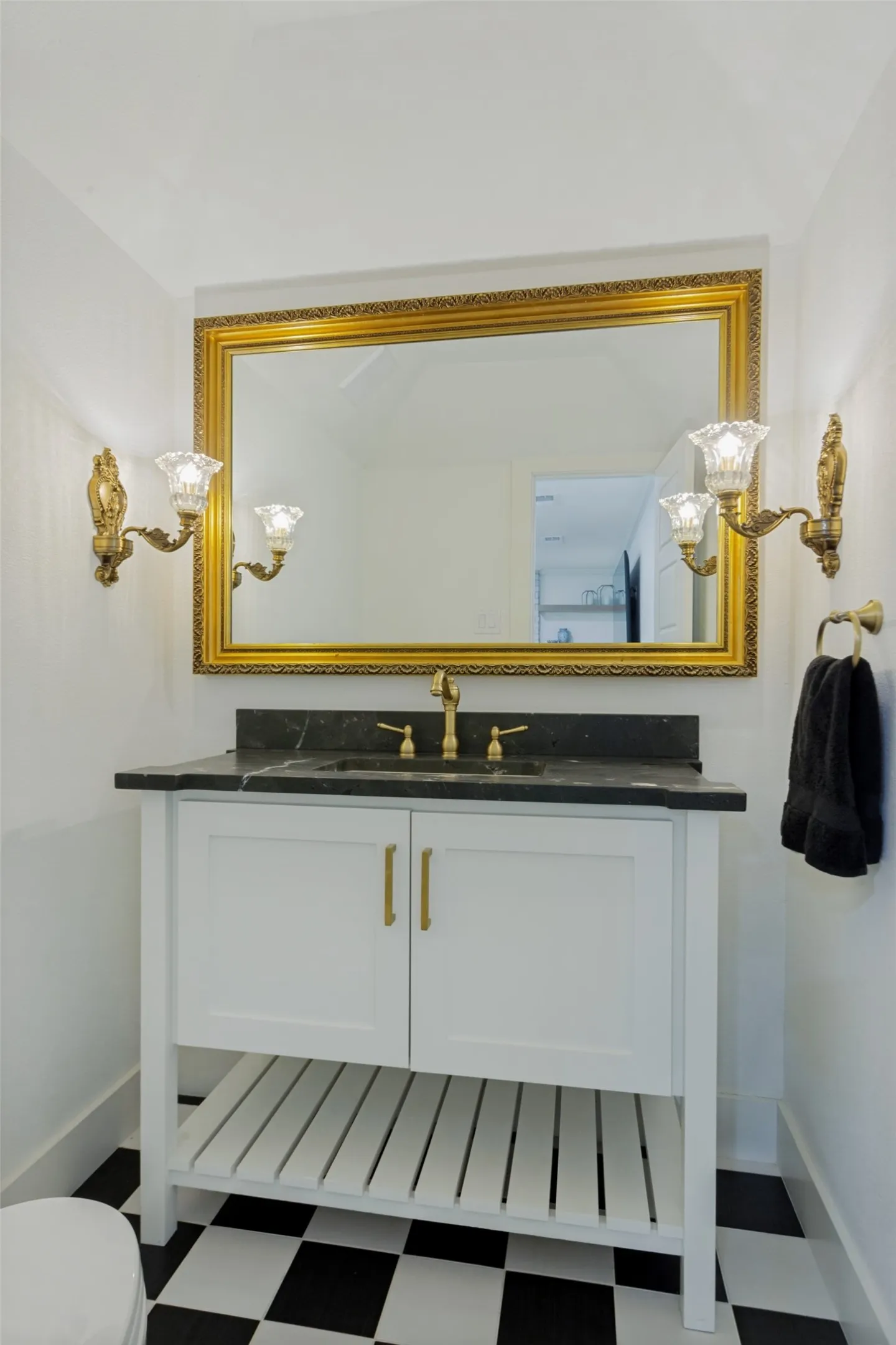 White vanity with gold-tone pulls, a dark countertop, and an undermount sink