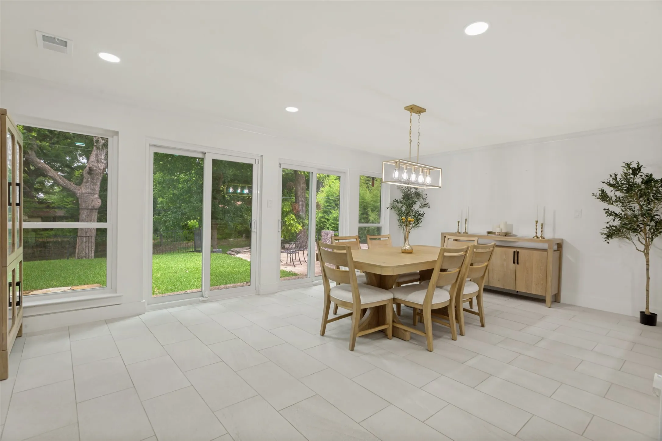 Bright, open dining area flooded with natural light through expansive multi-panel glass doors and windows overlooking manicured grounds
