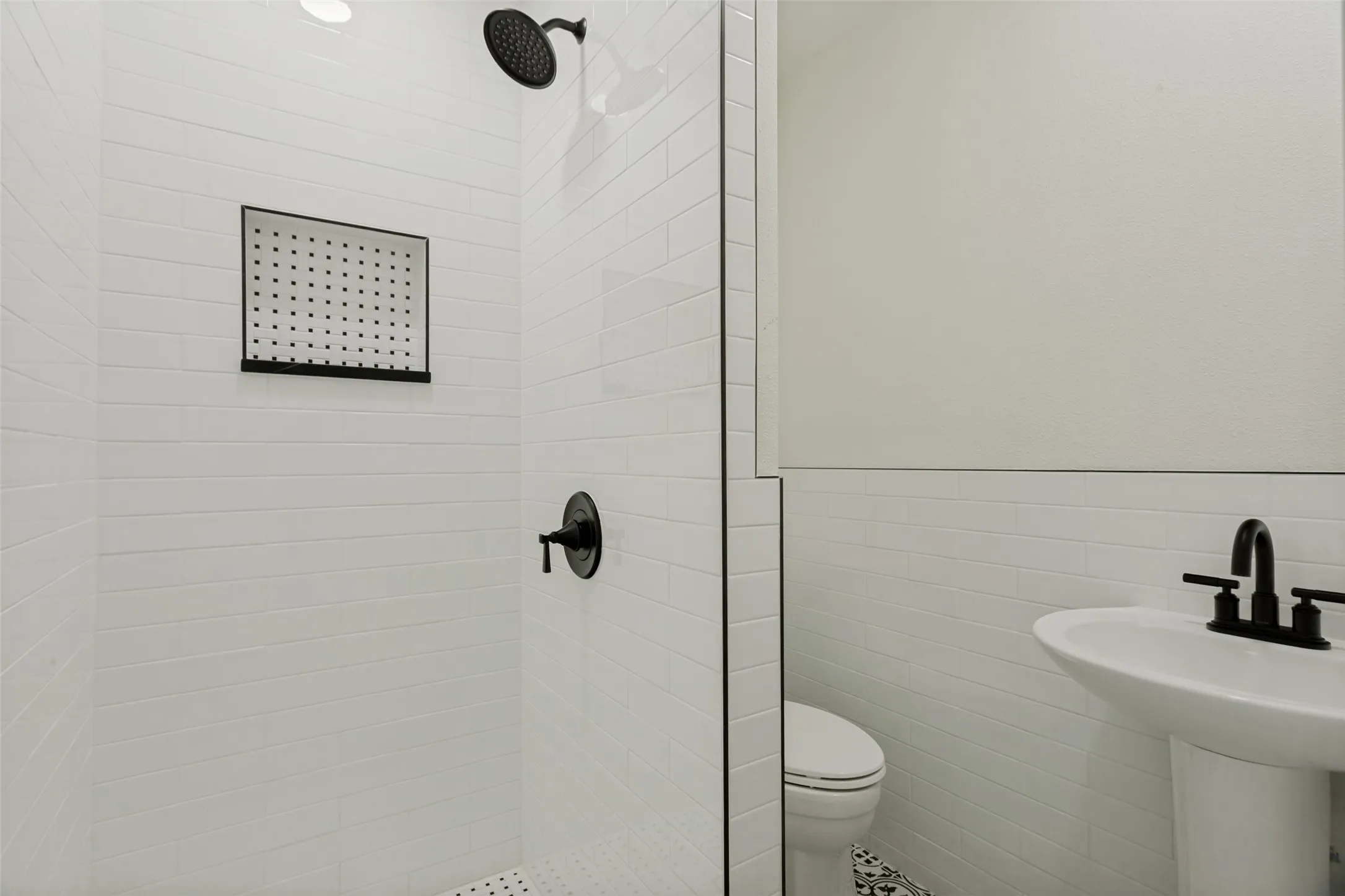 White subway tile shower with a matte black rain shower head and built-in niche