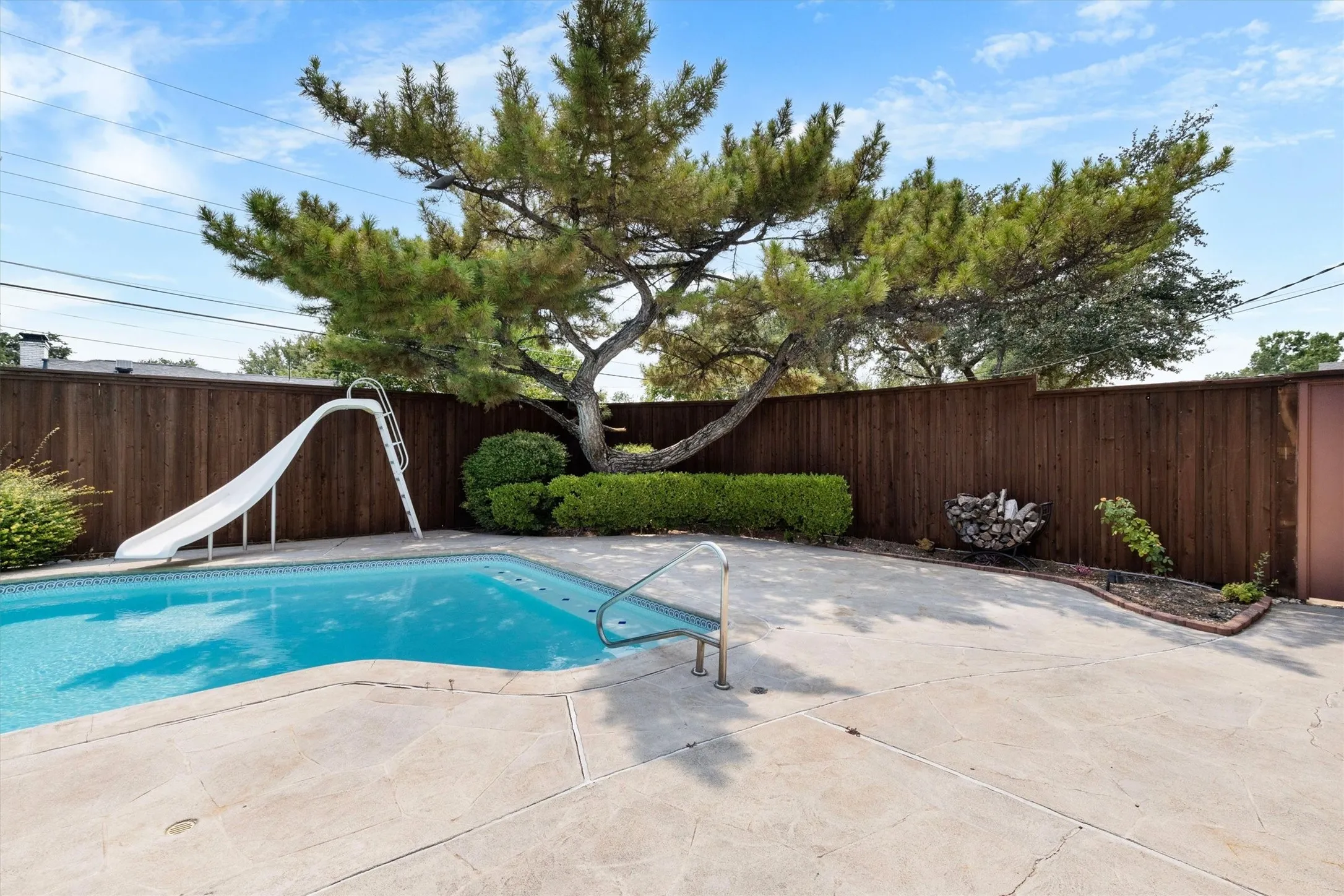 Private backyard featuring a swimming pool with a slide, concrete pool decking, and 8 ft wood privacy fencing