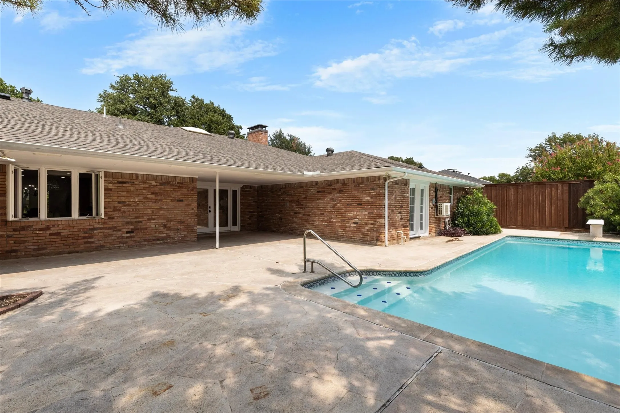 Covered patio, concrete pool deck, fenced perimeter, and inground swimming pool with integrated steps