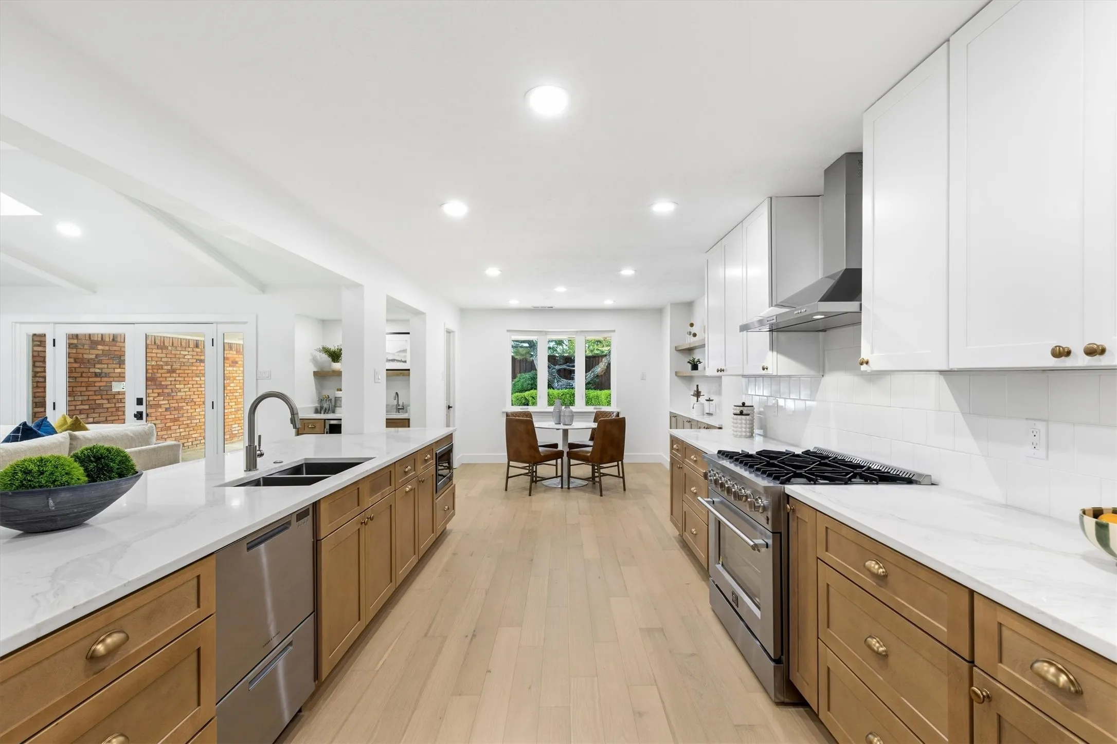 Expansive kitchen island with an integrated sink, stainless steel appliances, white cabinetry, and light wood-finish flooring