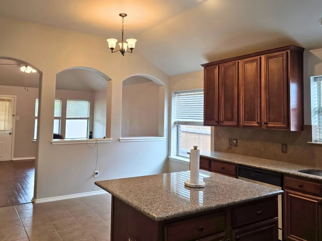Kitchen featuring a center island, wood-finish cabinetry, speckled countertops, and tile backsplash