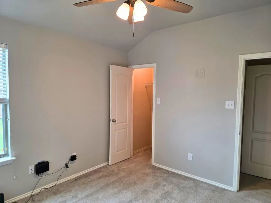 Room featuring neutral-toned walls, gray carpeting, a window with horizontal blinds, and a ceiling fan with integrated lighting