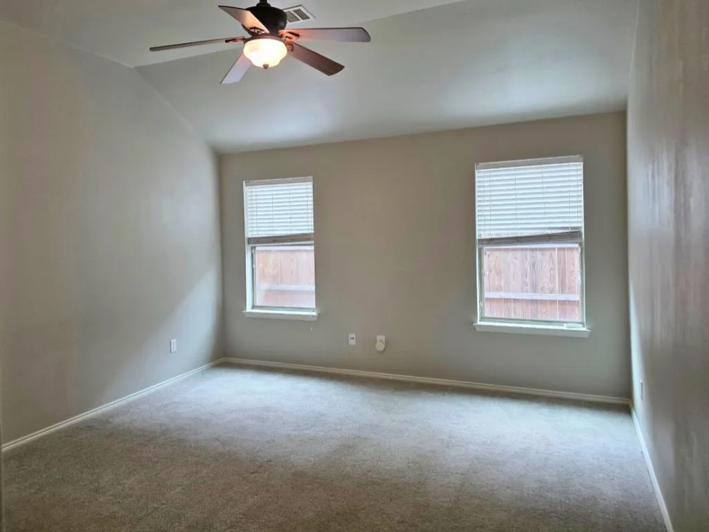 Carpeted interior space featuring neutral wall tones, two windows with blinds, a ceiling fan with integrated lighting, and crown molding