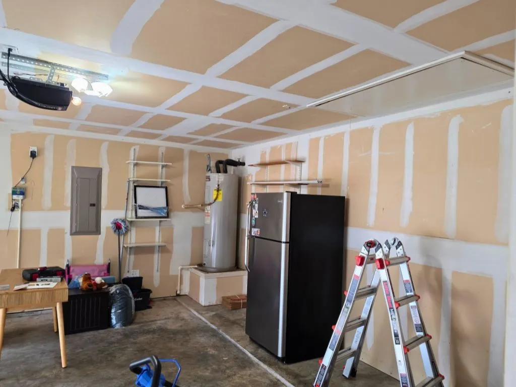 Spacious garage featuring a concrete floor, exposed drywall with taped seams, built-in shelving, and an overhead garage door opener with integrated lighting