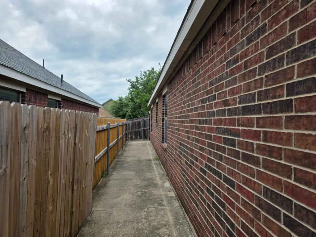 Brick exterior featuring a concrete walkway and a wood privacy fence