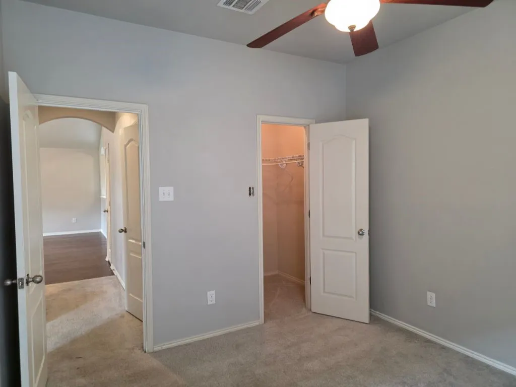 Carpeted room featuring a ceiling fan with integrated lighting, a walk-in closet with wire shelving, and an arched doorway leading to an area with wood-finish flooring