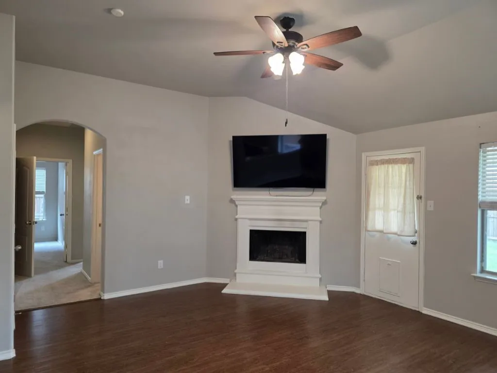 Spacious living area featuring wood-finish flooring, a white mantel fireplace, and a ceiling fan with light fixture