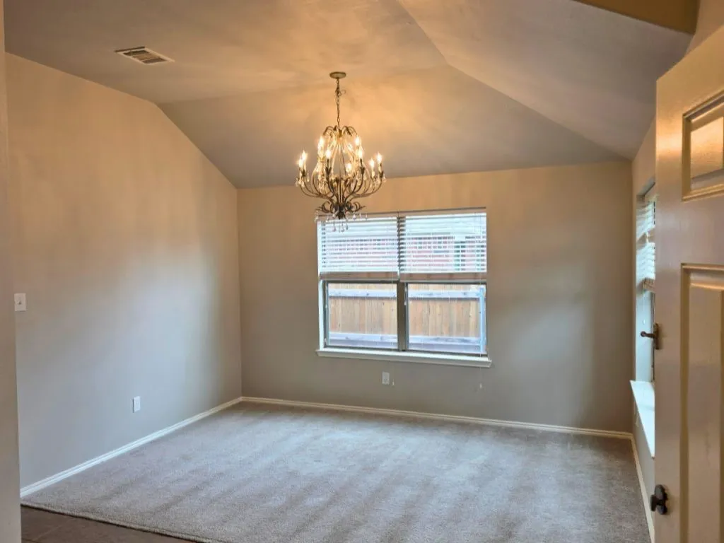 Vaulted ceiling room featuring a multi-bulb chandelier, neutral tone carpet, and a large window with blinds