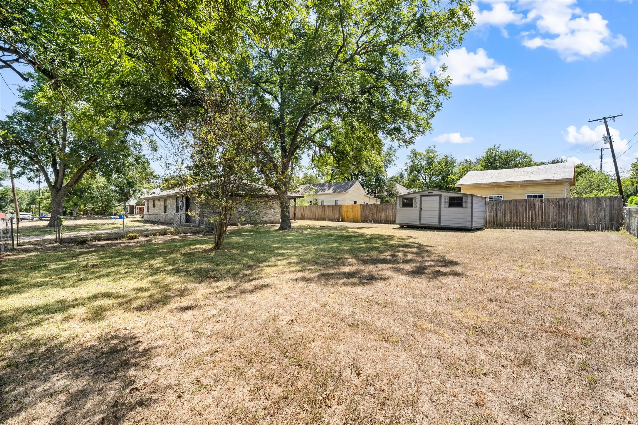Expansive outdoor space featuring a detached storage shed, mature trees, and a wood privacy fence