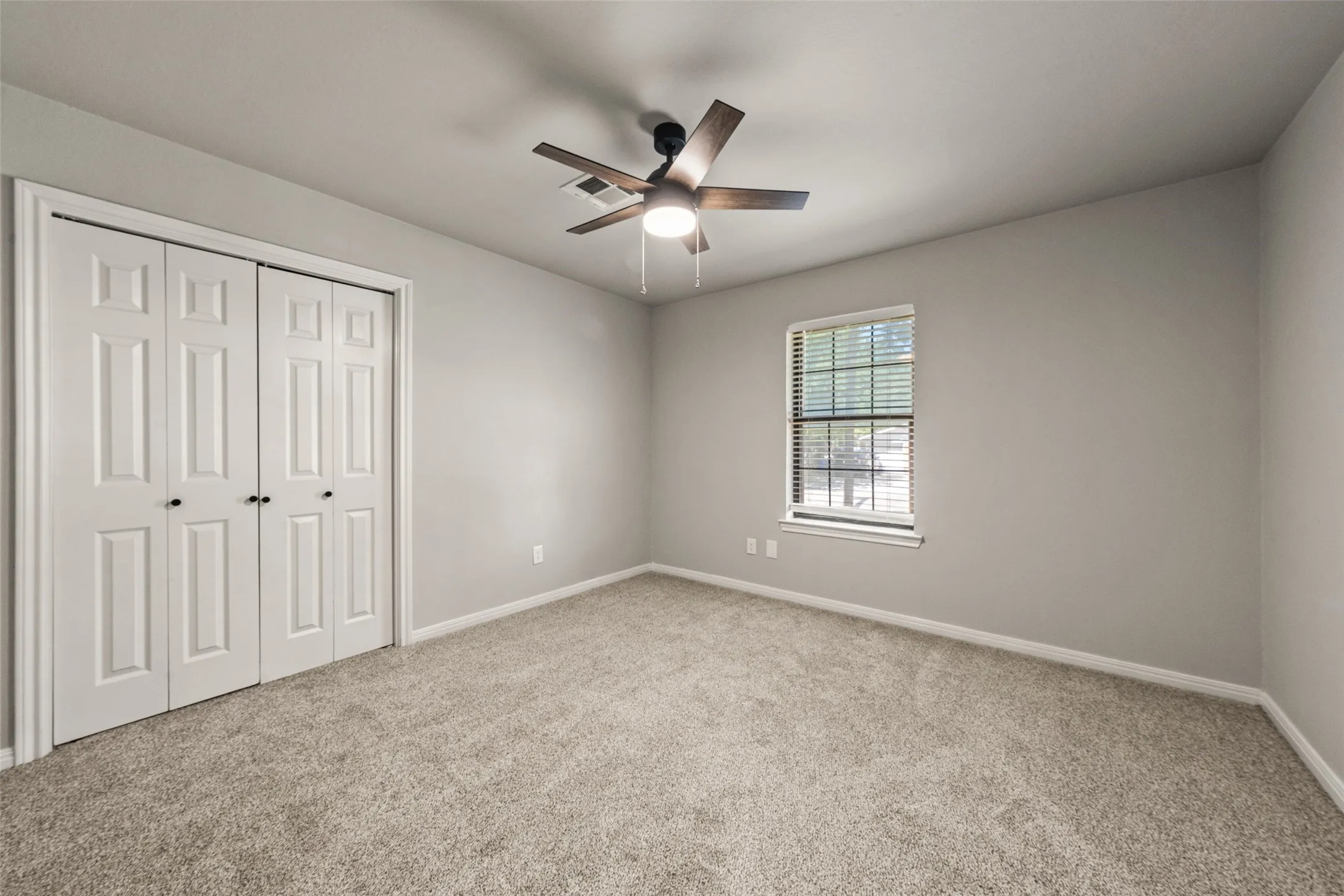 Gray wall finishes, carpet flooring, a window with blinds, and a ceiling fan with integrated lighting