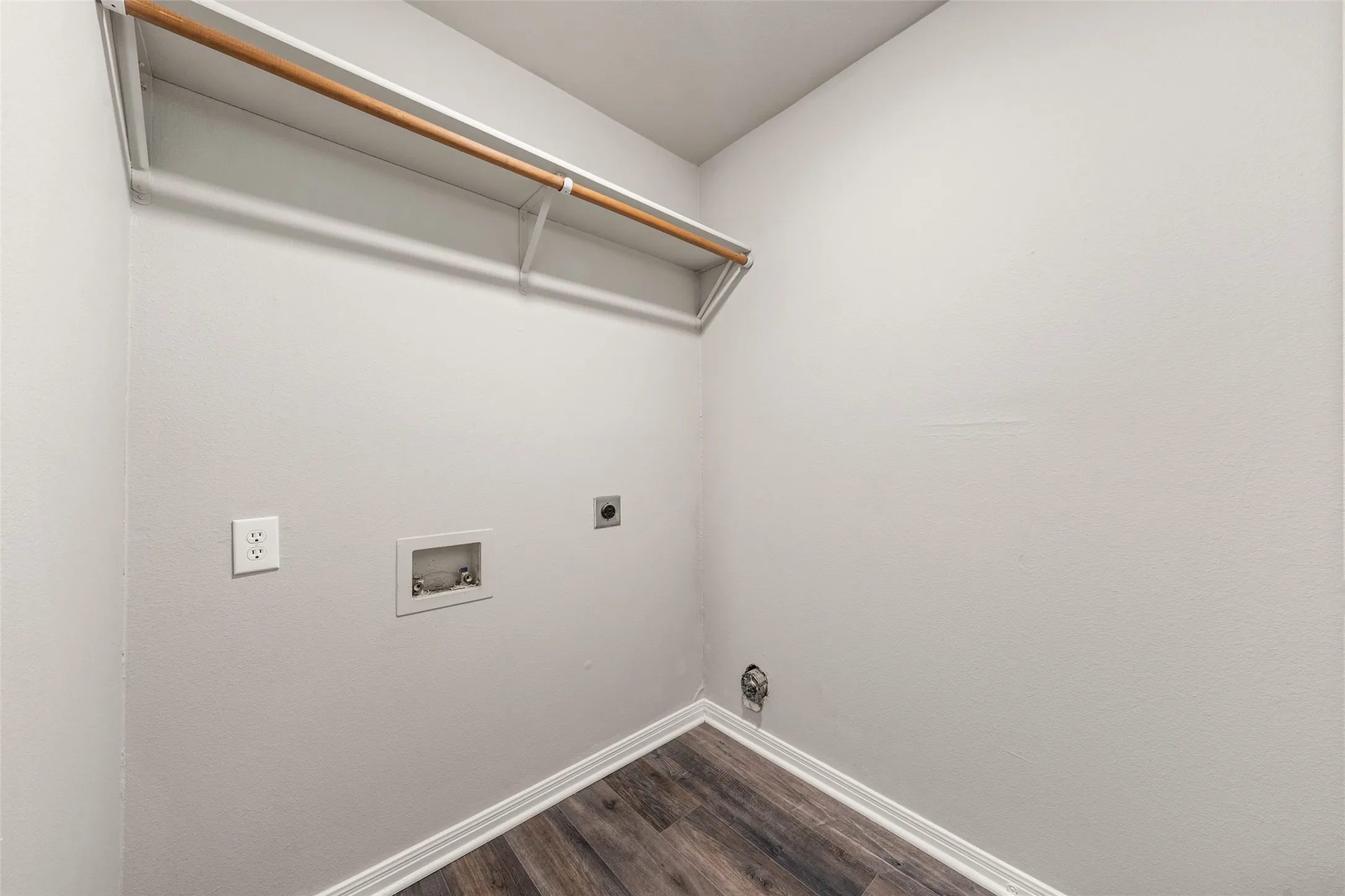 Laundry area featuring wood-finish flooring, white walls, and a built-in storage shelf with a hanging rod
