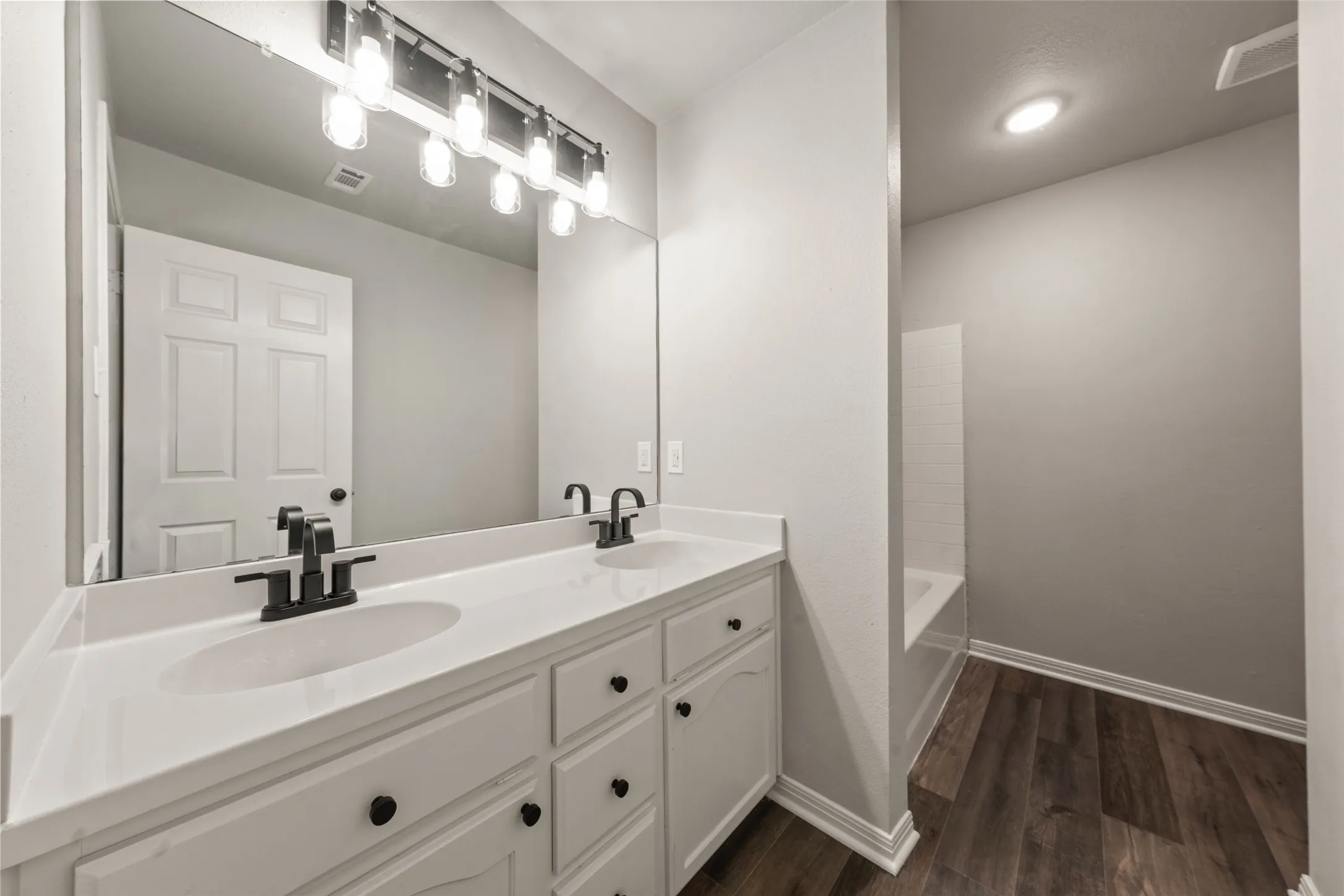 Dual vanity with white cabinetry, matte black fixtures, and a spacious mirror
