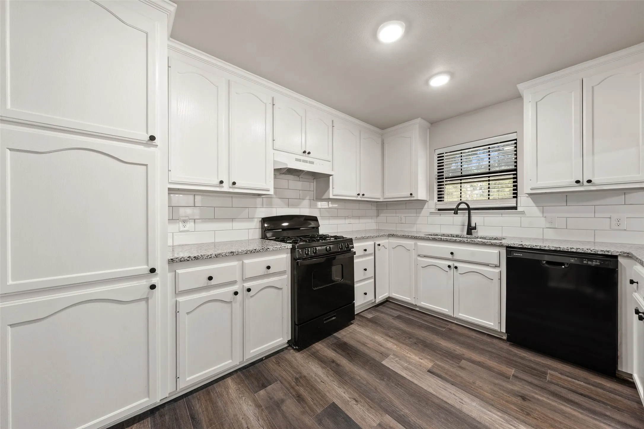 Kitchen featuring wood-finish flooring, white cabinetry, granite-style countertops, subway tile backsplash, and recessed lighting